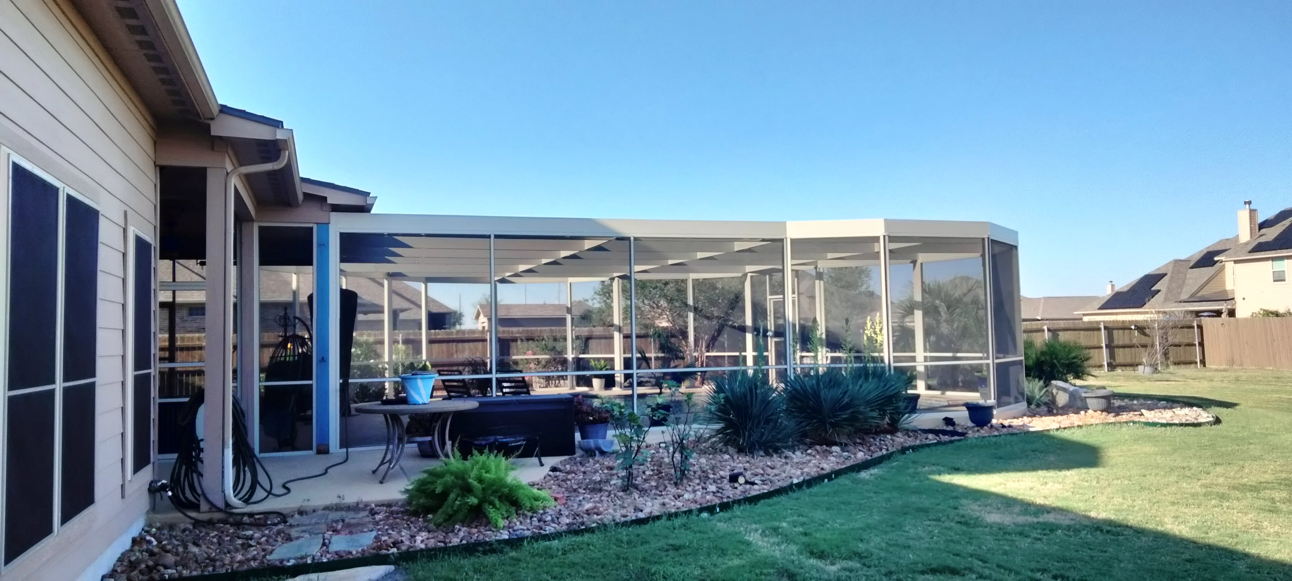White aluminum patio enclosure with retractable screens, shade panels, and landscaping