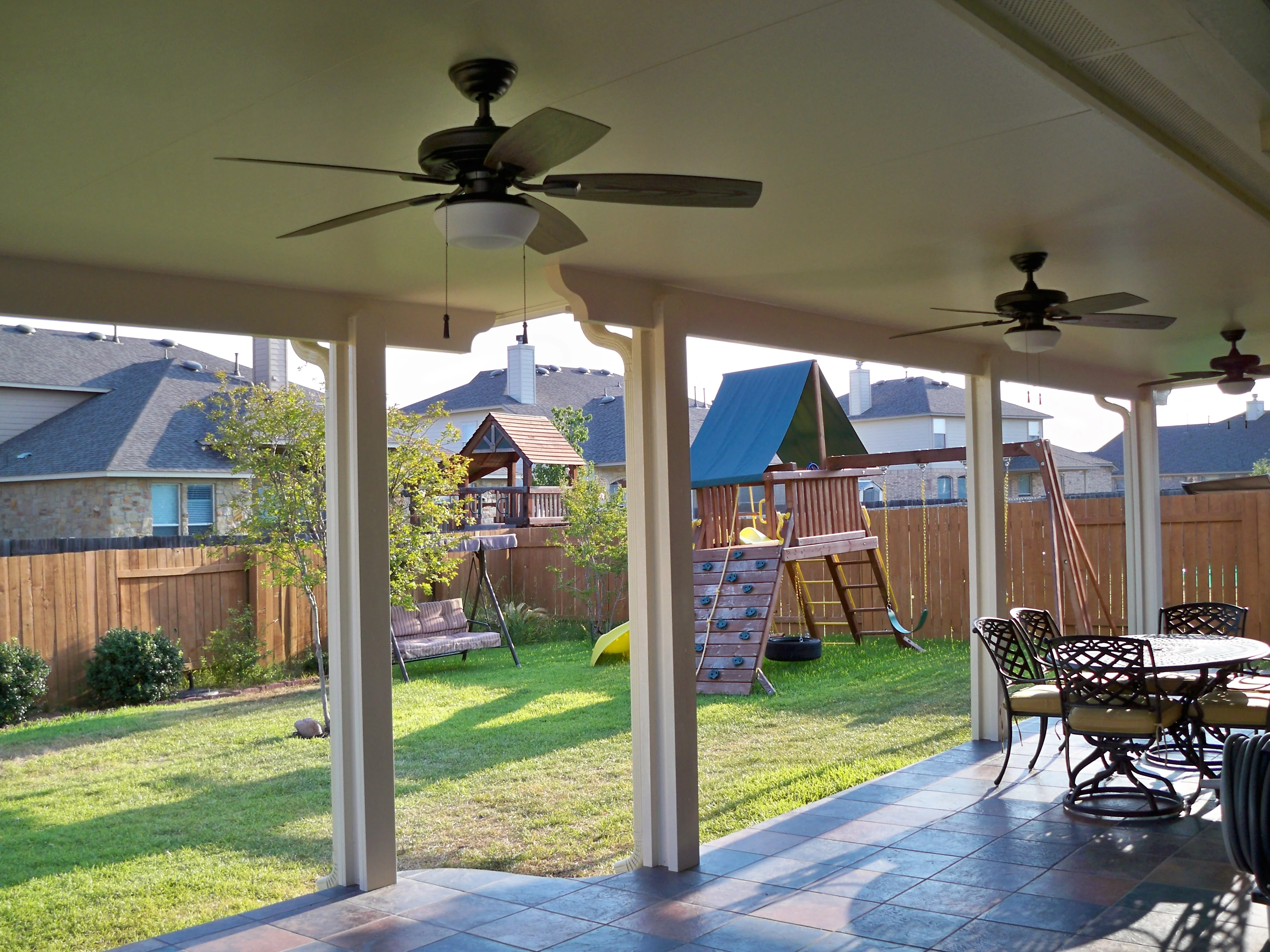 Covered patio with white columns, ceiling fans, tile flooring, and open backyard views