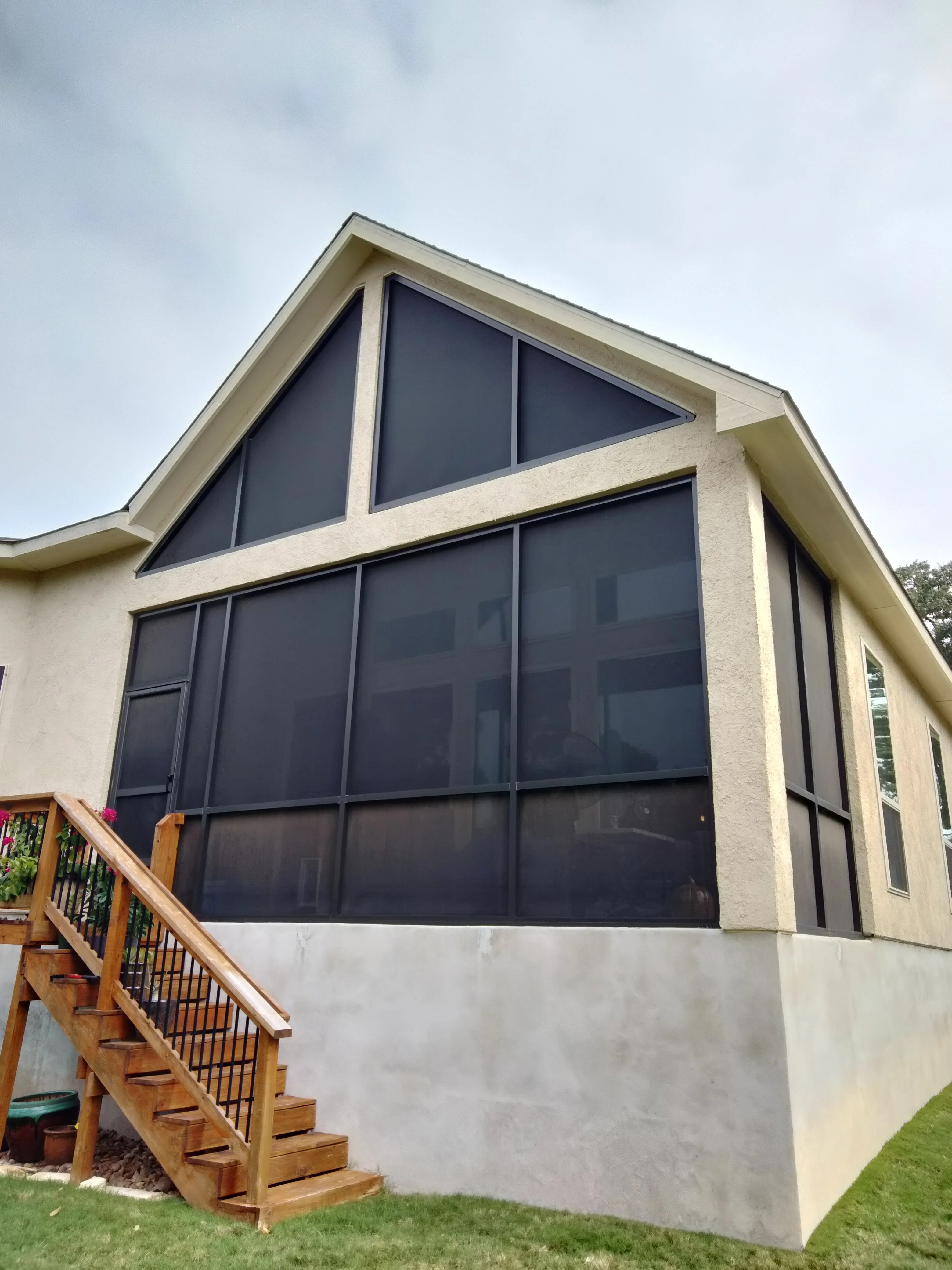 Dark-tinted glass patio enclosure with aluminum frame and gable roof on concrete foundation