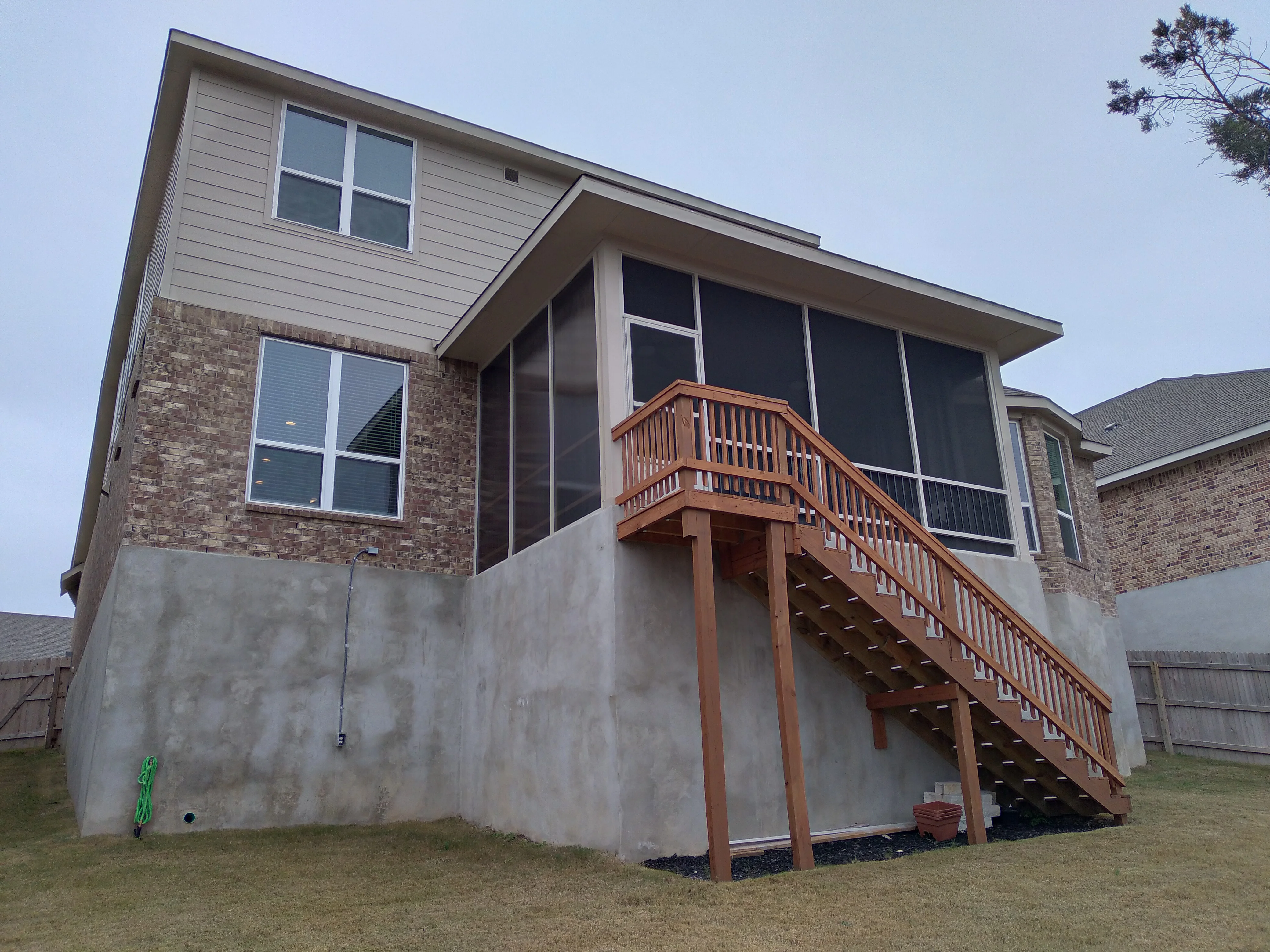Screened patio enclosure with large windows, cedar deck, and staircase on brick home