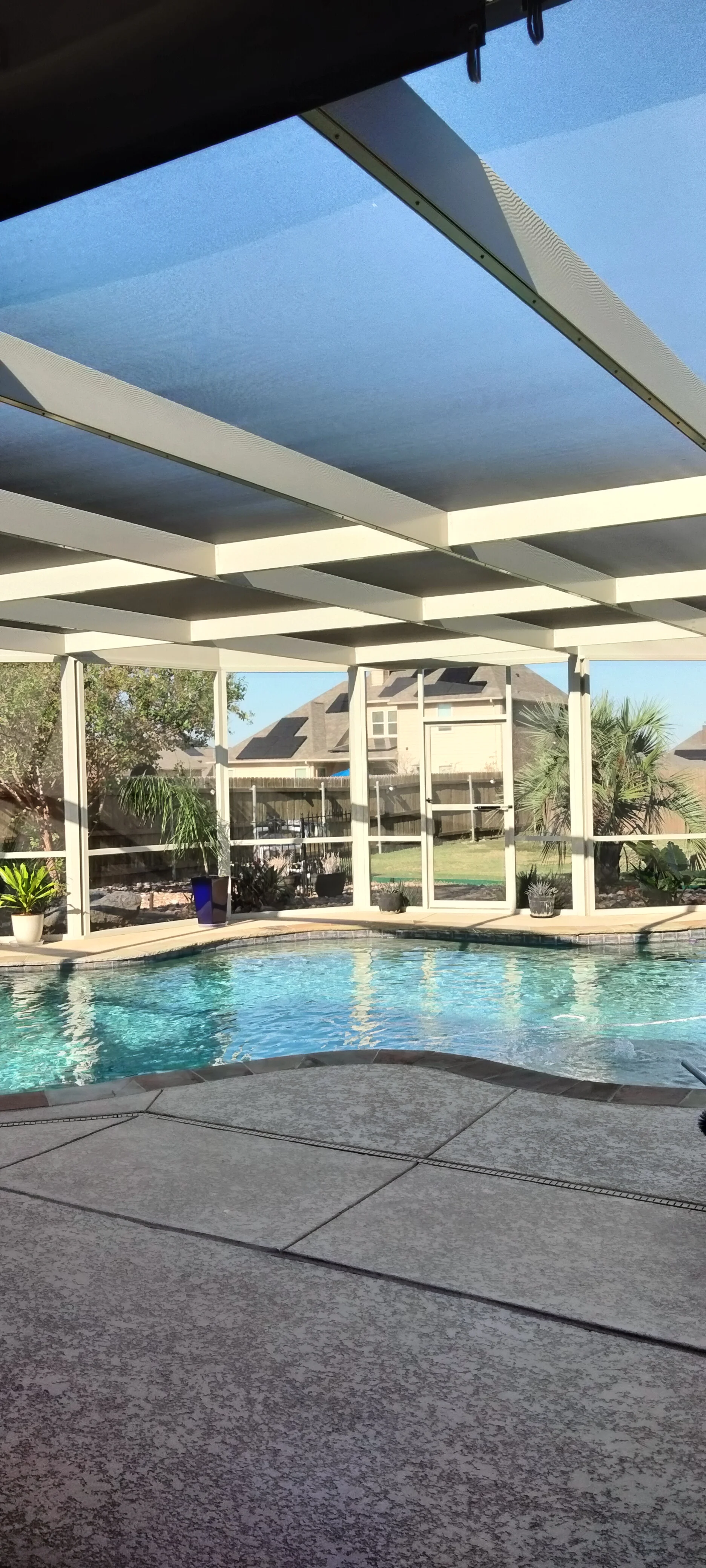 White aluminum patio frame with retractable blue shade fabric over swimming pool and concrete deck