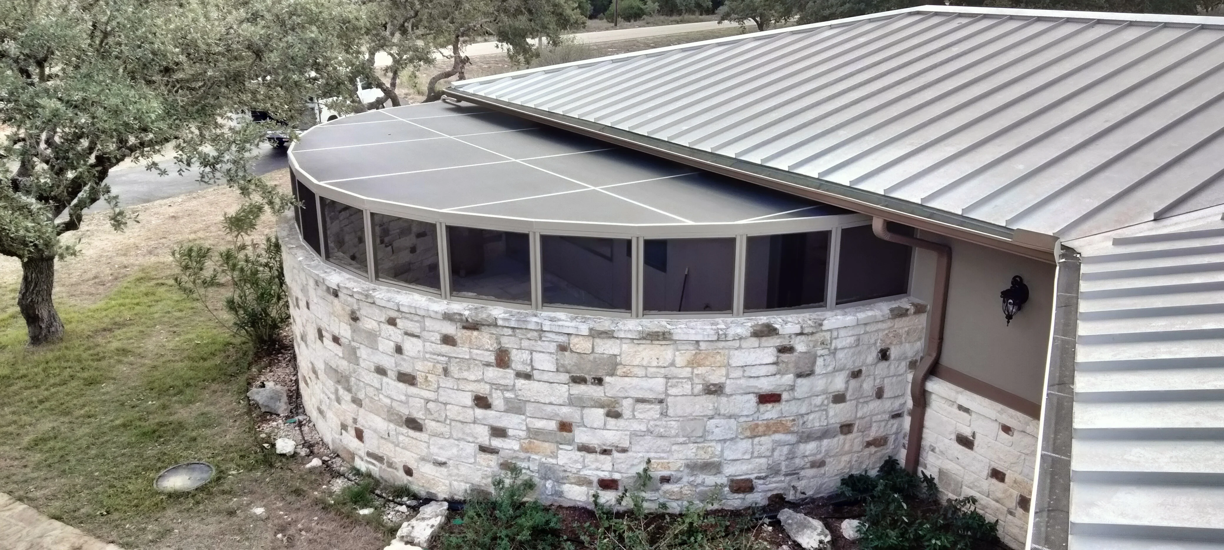 Curved stone patio enclosure with standing seam metal roof and multi-pane windows