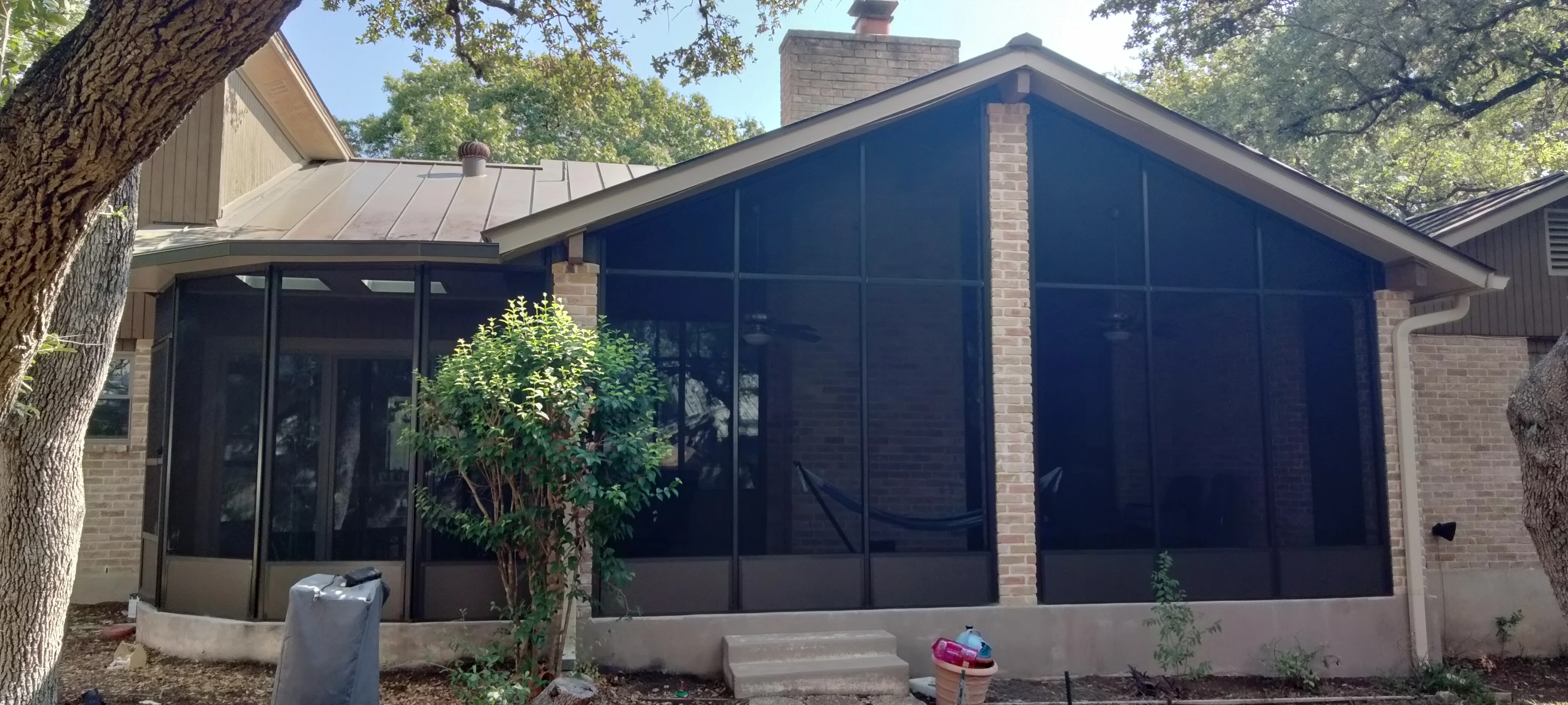 Black aluminum patio enclosure with glass panels, brick columns, and metal roof