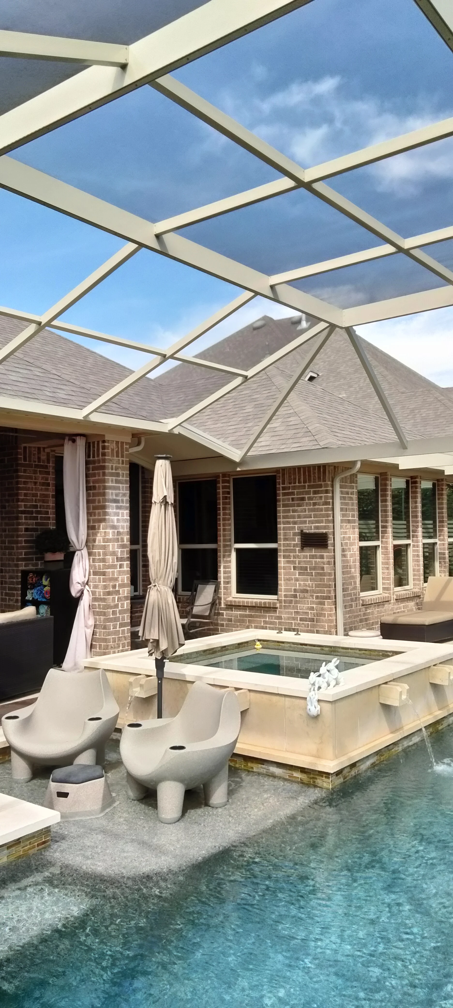 Glass roof patio enclosure with aluminum frame over pool deck and brick home