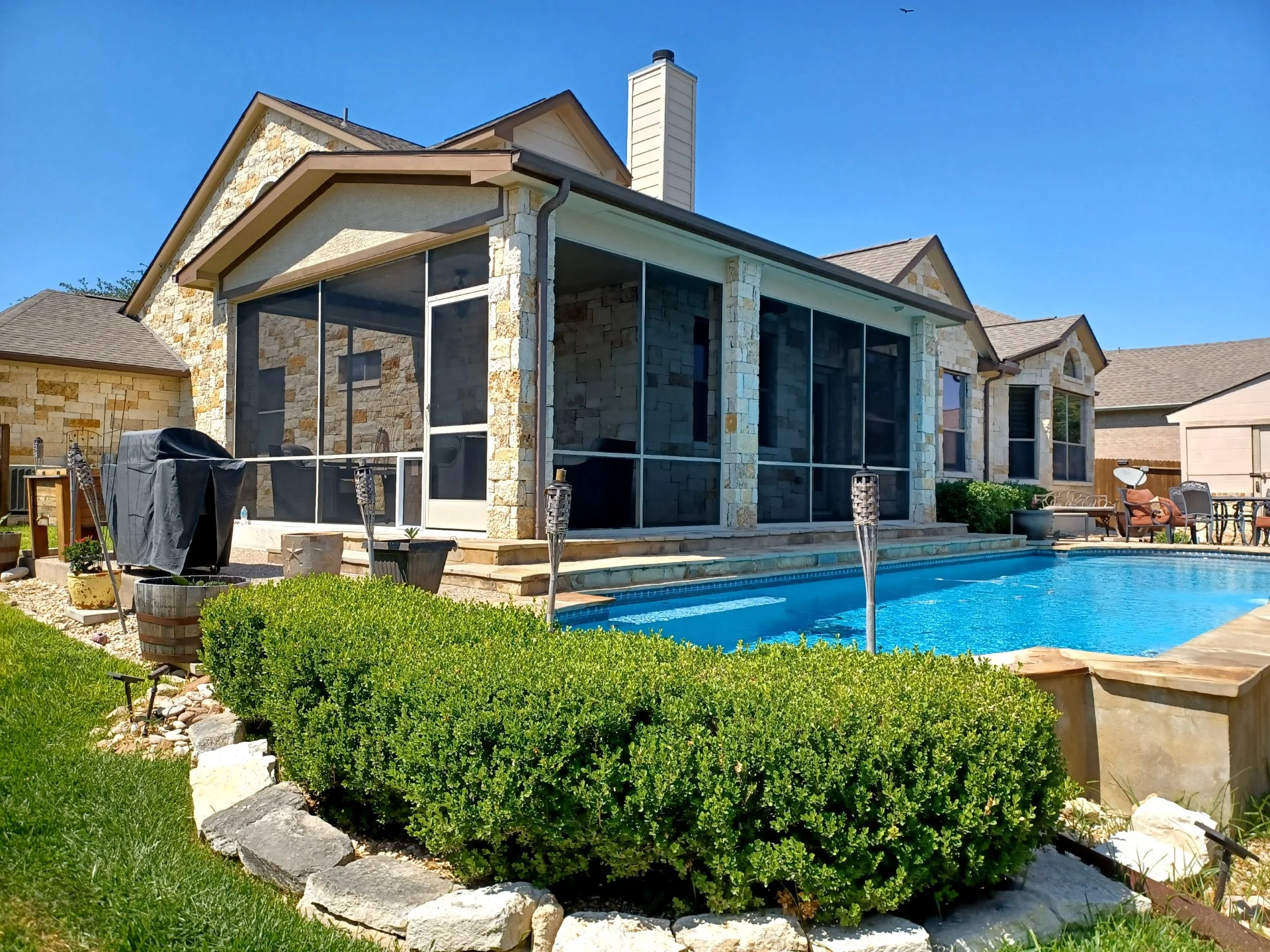 Screened patio enclosure with aluminum frame, dark mesh screening, and stone veneer exterior