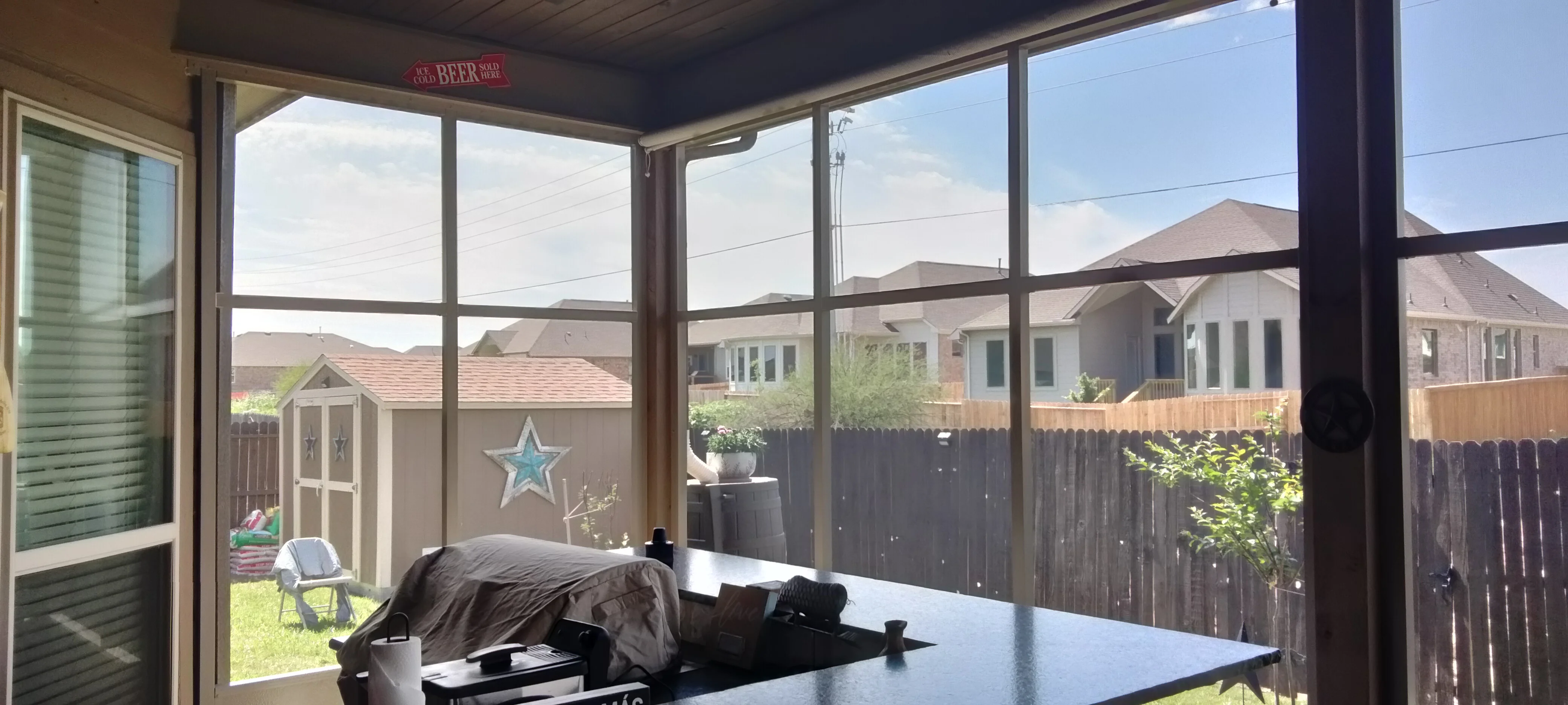 Aluminum patio enclosure with glass sliding doors and roof, overlooking fenced backyard
