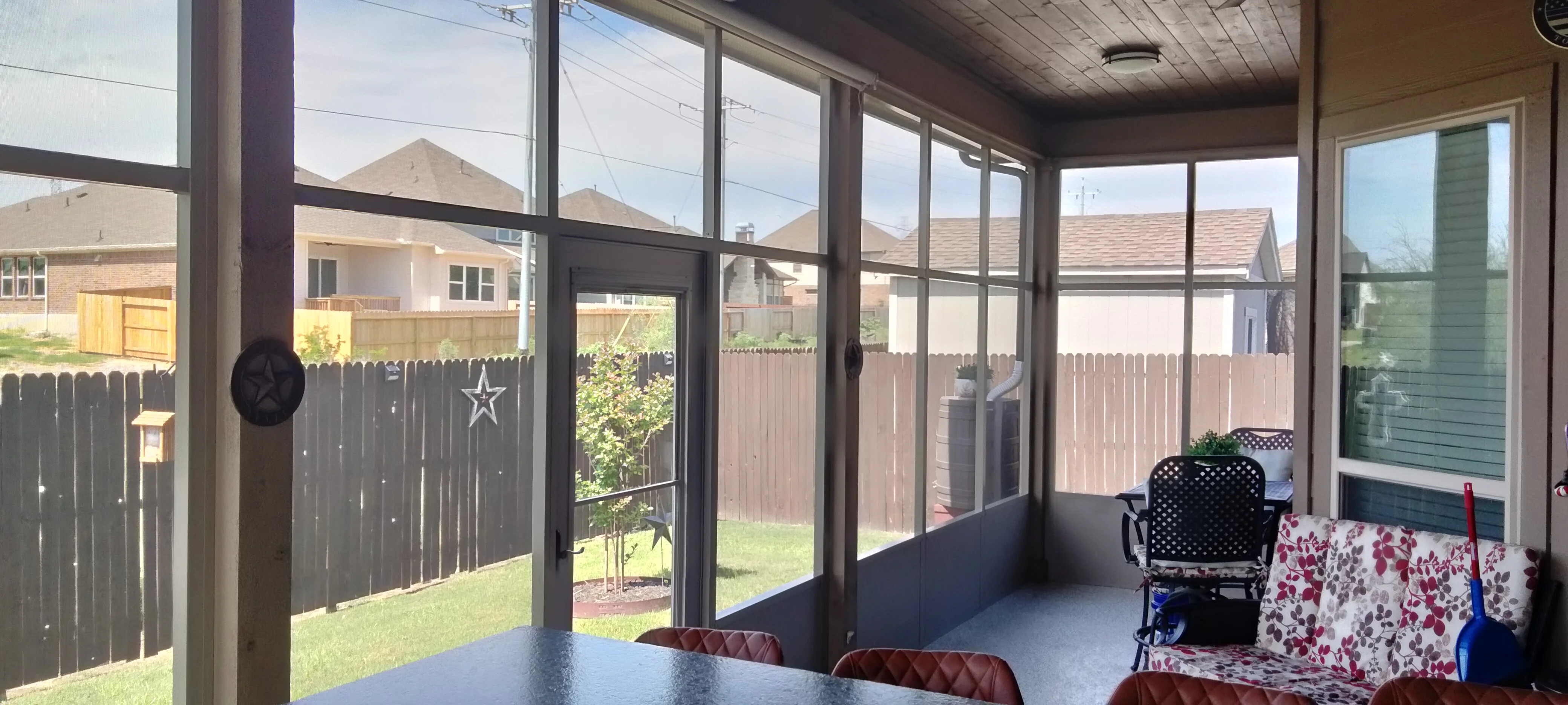 Screened patio with aluminum frame, glass doors, and dark metal posts overlooking fenced yard