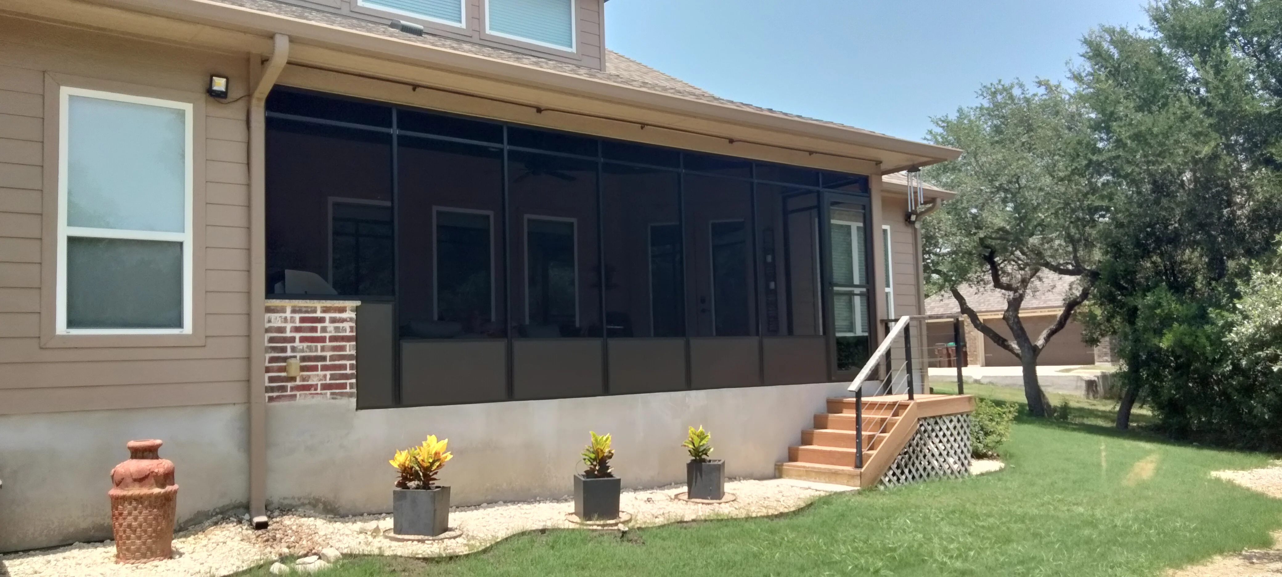 Black screened patio enclosure with concrete foundation, brick steps, and metal railings attached to brick home