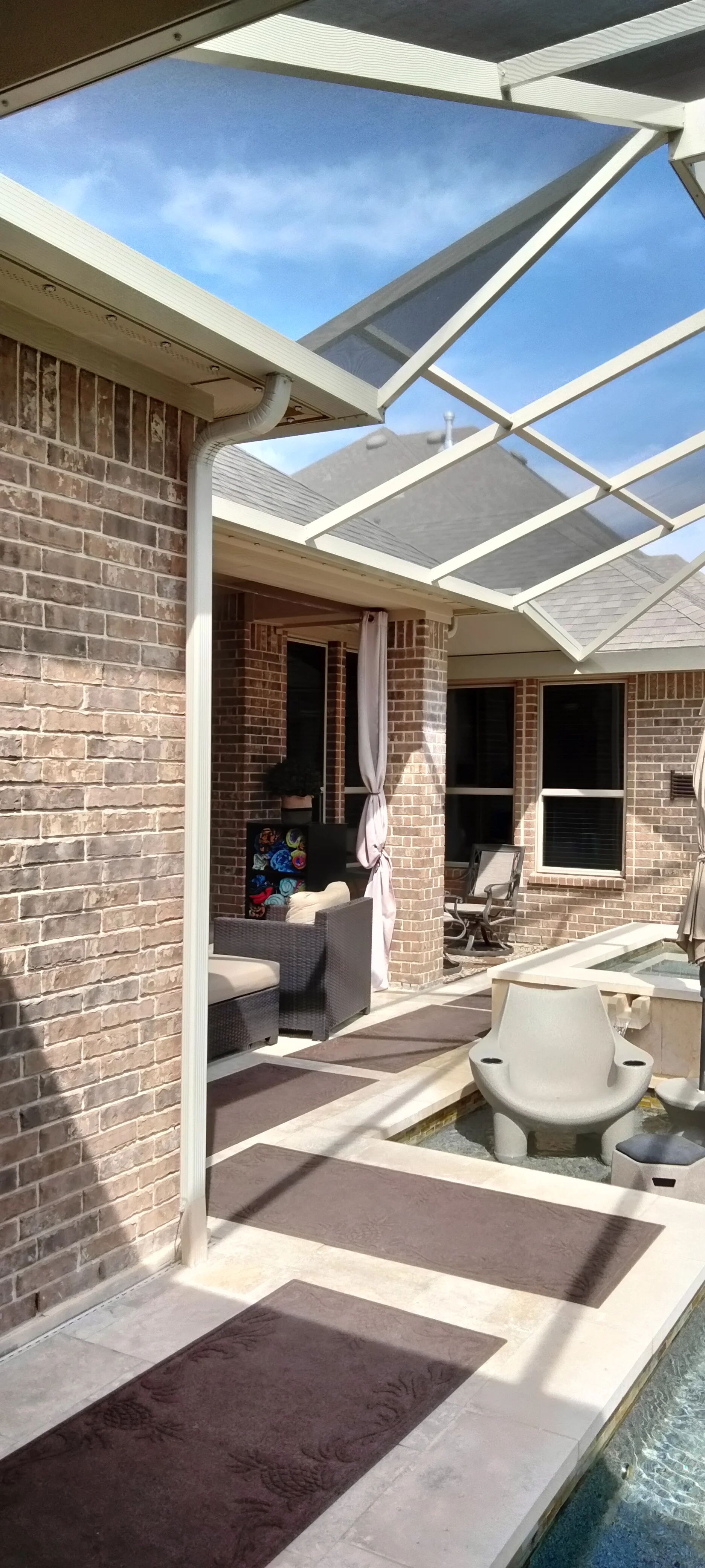 White aluminum patio enclosure with polycarbonate roof panels over brick home exterior