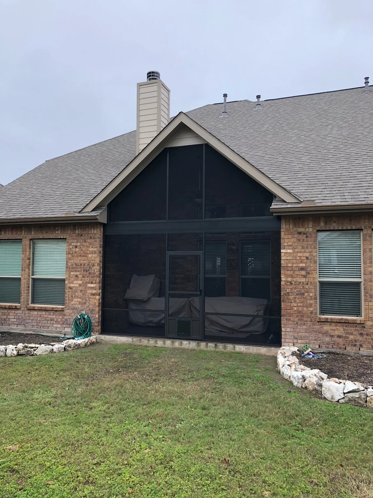 Black aluminum patio enclosure with glass panels on brick home exterior