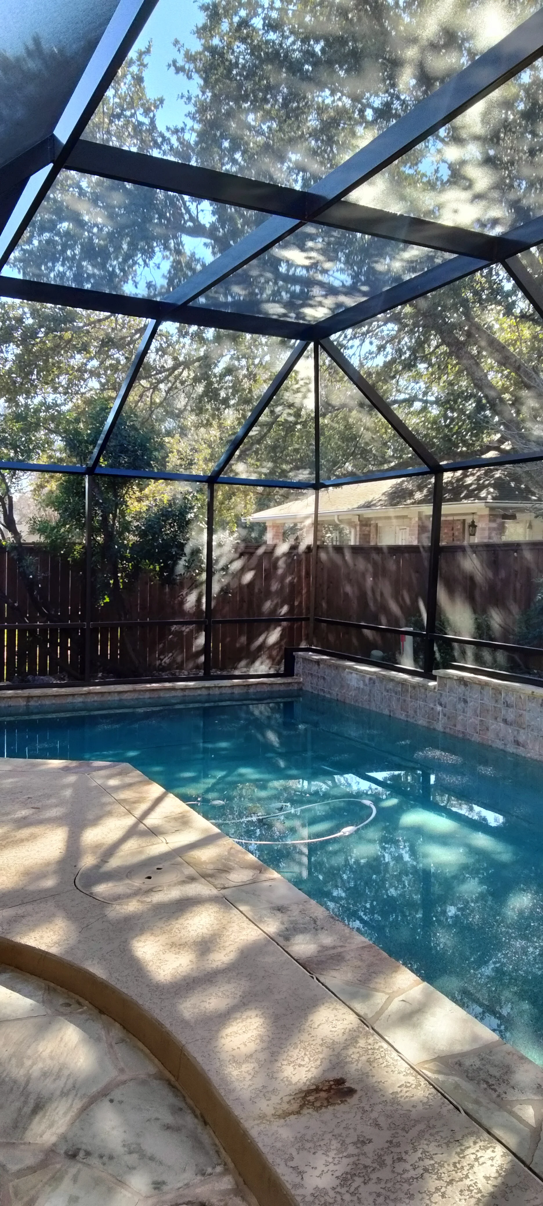 Aluminum and glass pool enclosure with clear roof panels over swimming pool and concrete deck