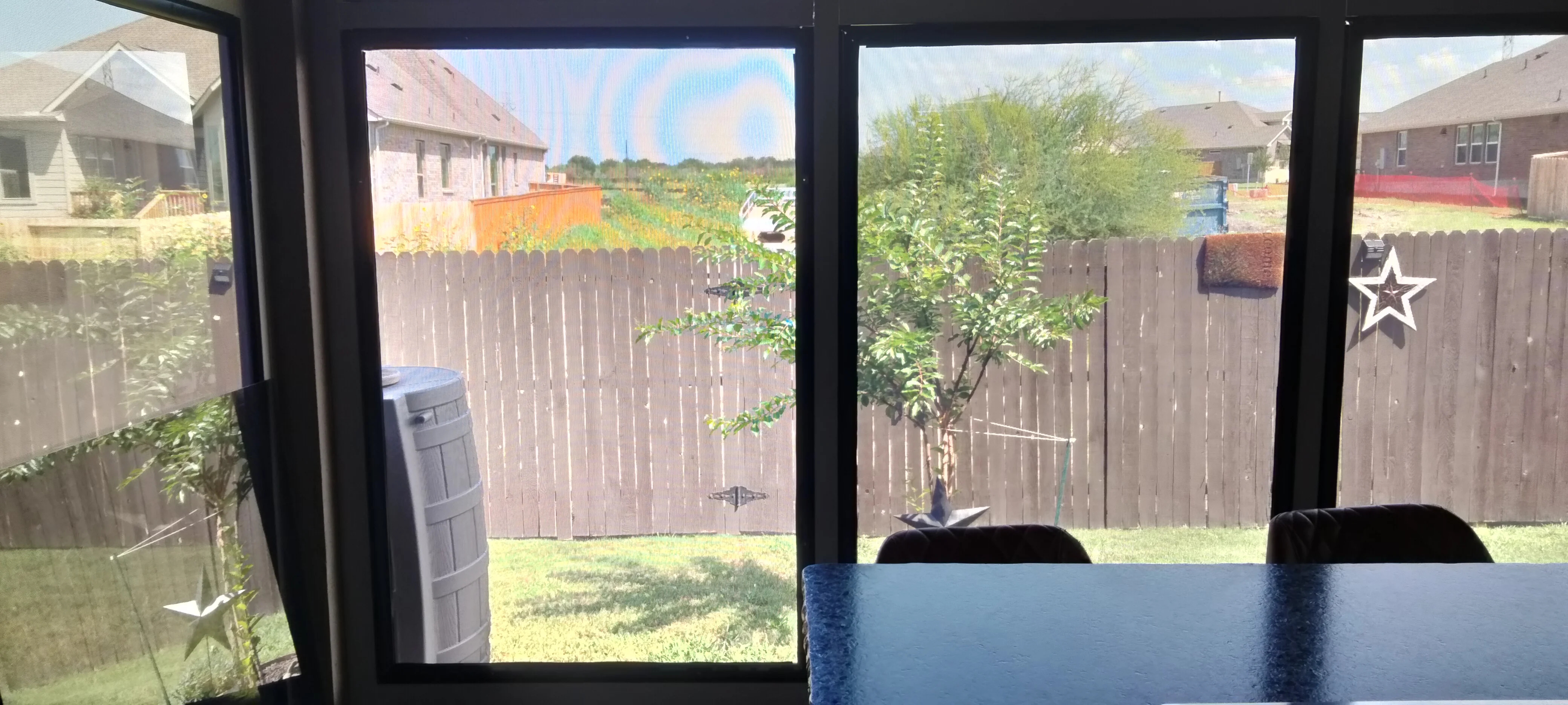 Patio enclosure with black-framed sliding glass doors overlooking fenced yard with grass and plantings