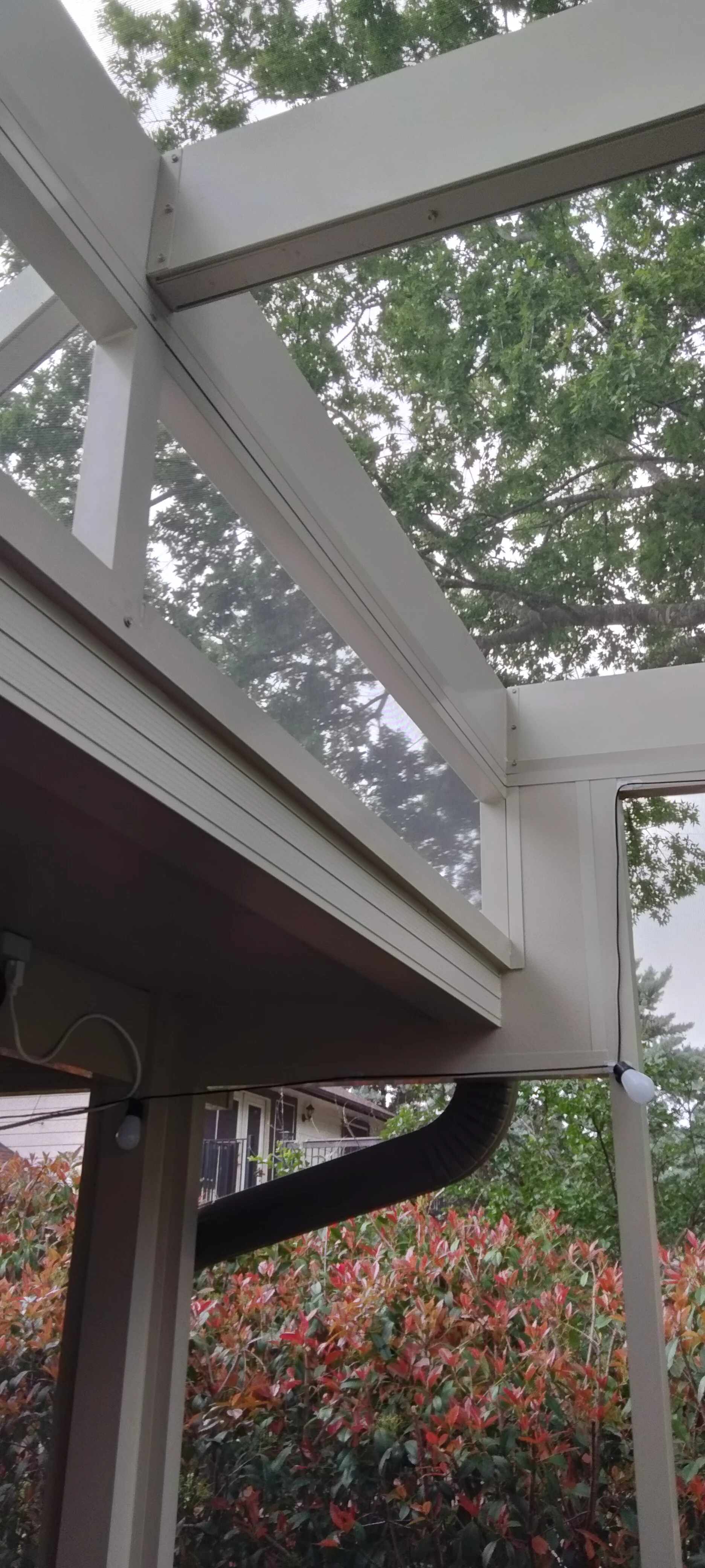 White aluminum pergola with skylight panels and dark metal support beams over garden landscape