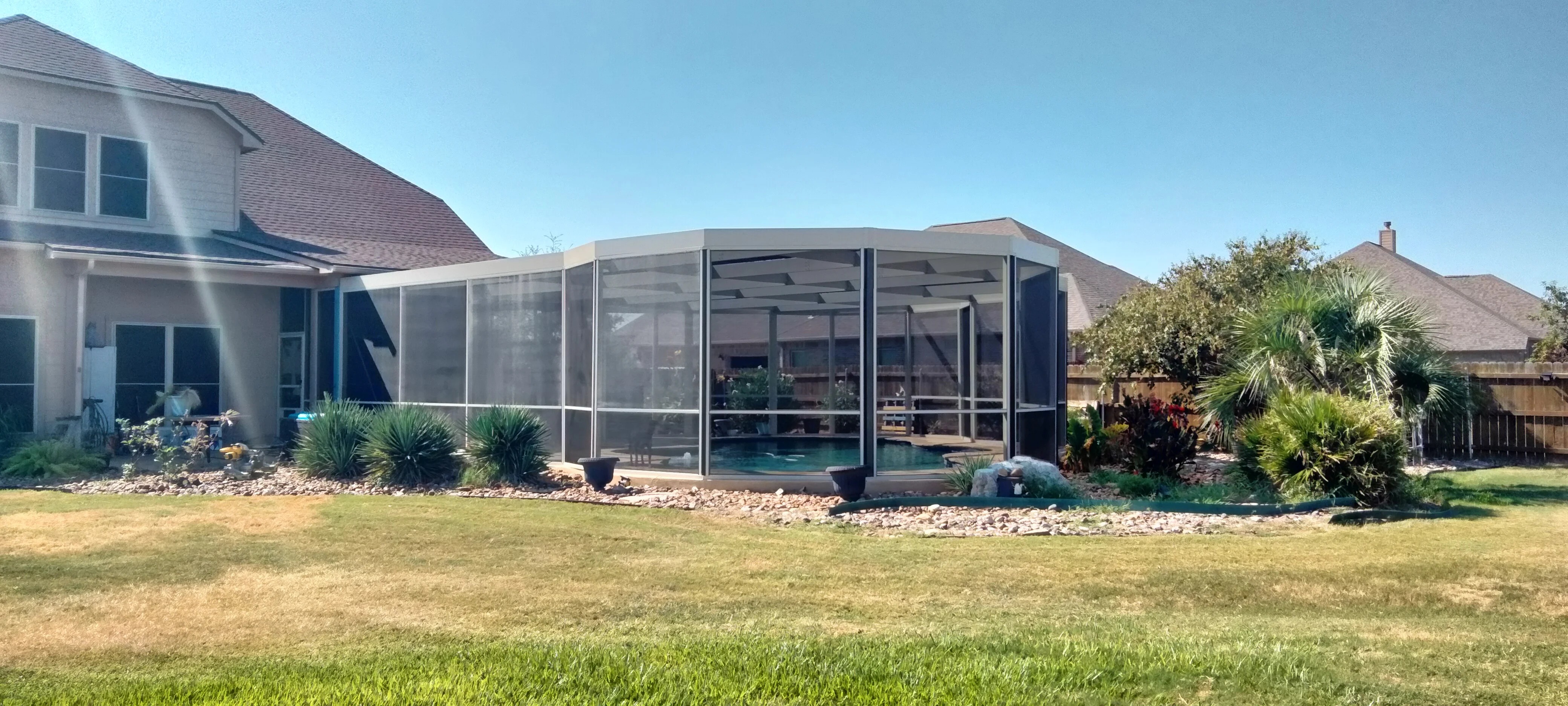 Aluminum pool enclosure with screen panels, insulated roof, and river rock landscaping