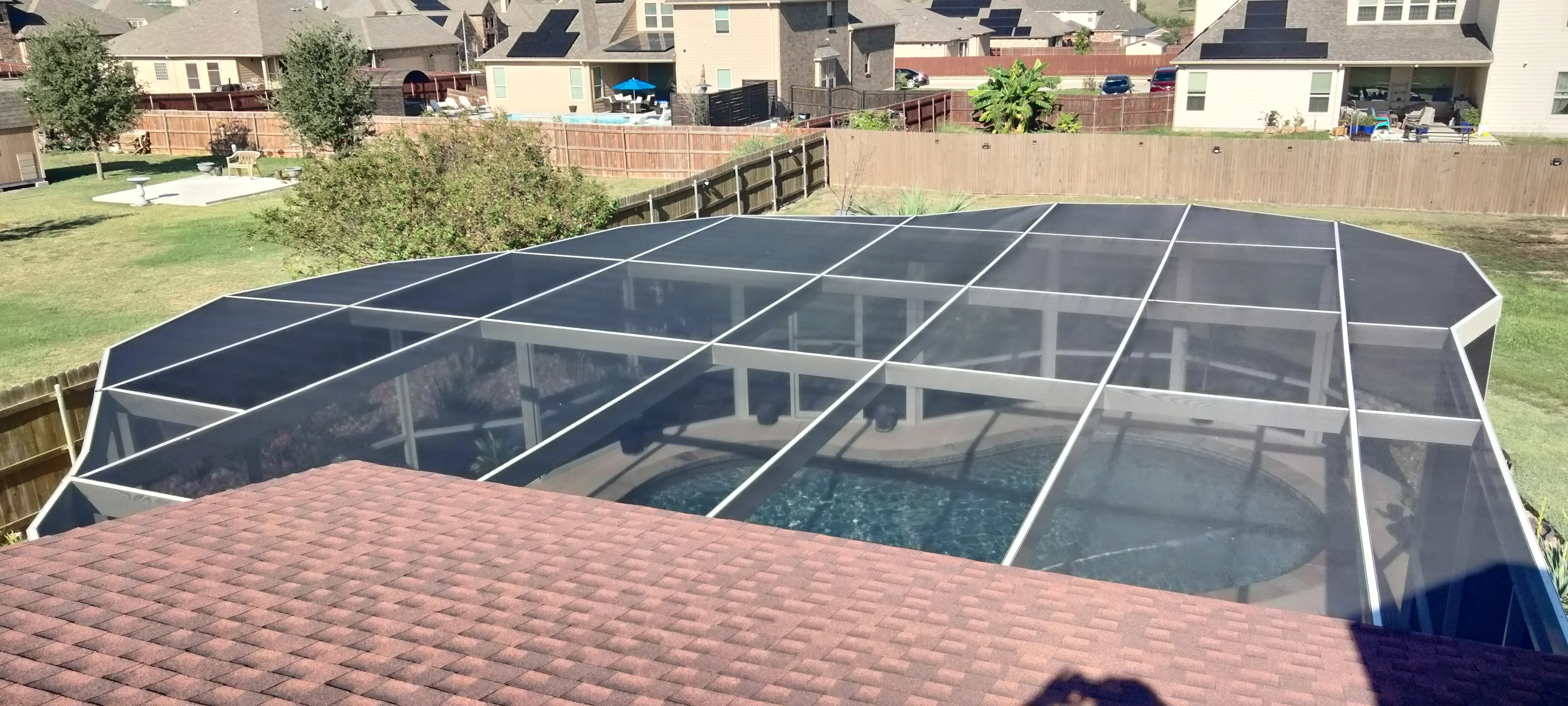 Dark-framed pool enclosure with glass panels and angled roof over residential pool and brick patio