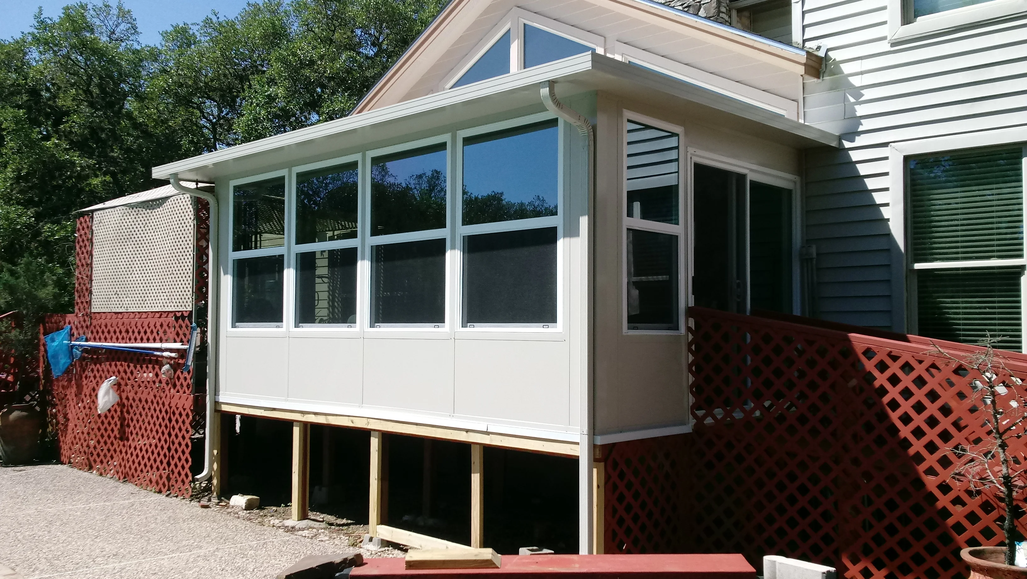 White aluminum-framed patio enclosure with multi-pane windows, pitched roof, and red lattice privacy panels