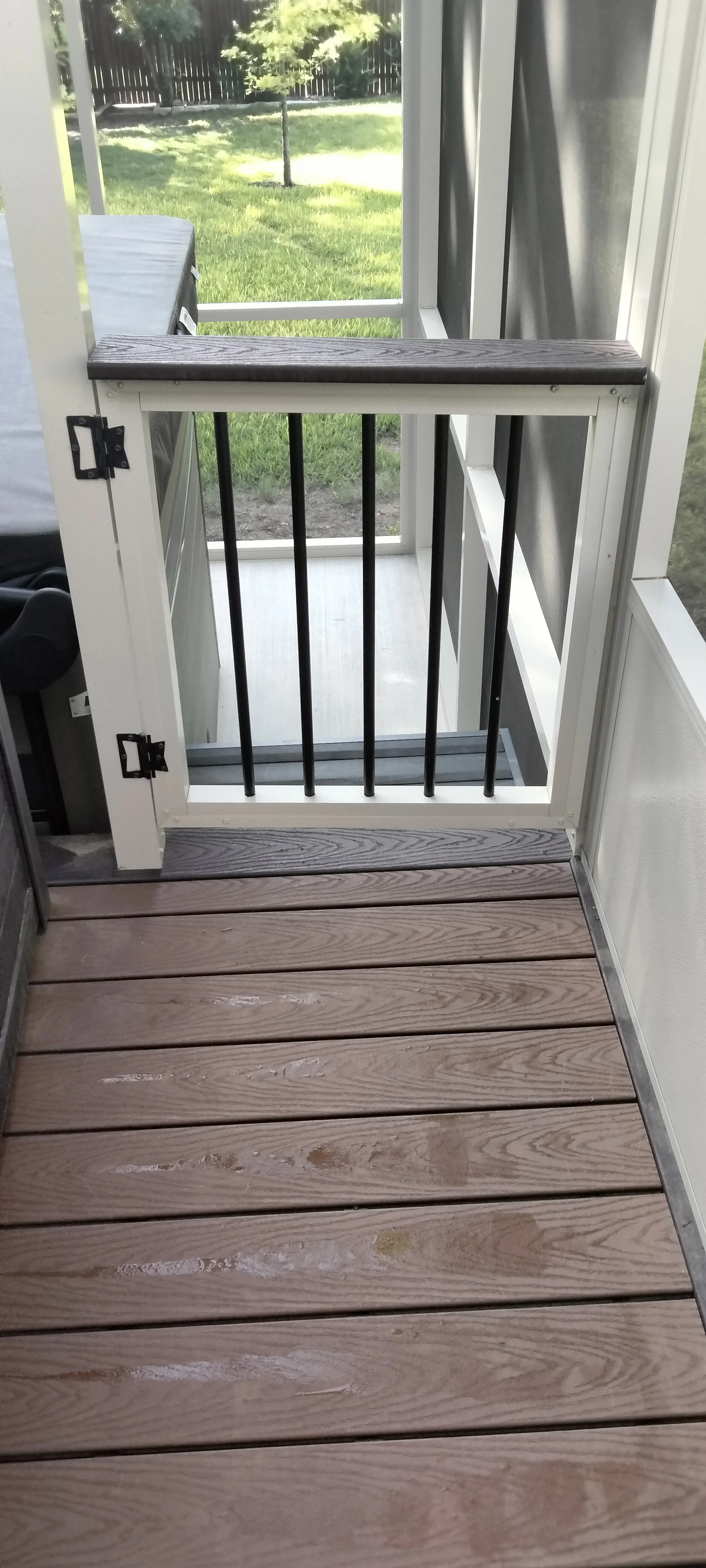 Black metal spindle pet gate on white frame installed on composite deck with wood-grain finish