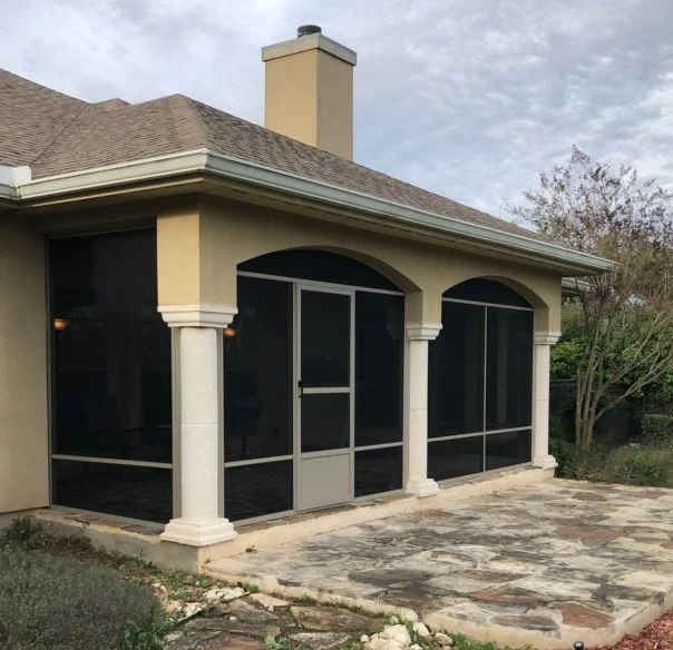 Patio enclosure with arched openings, white columns, black screens, and stone paver flooring