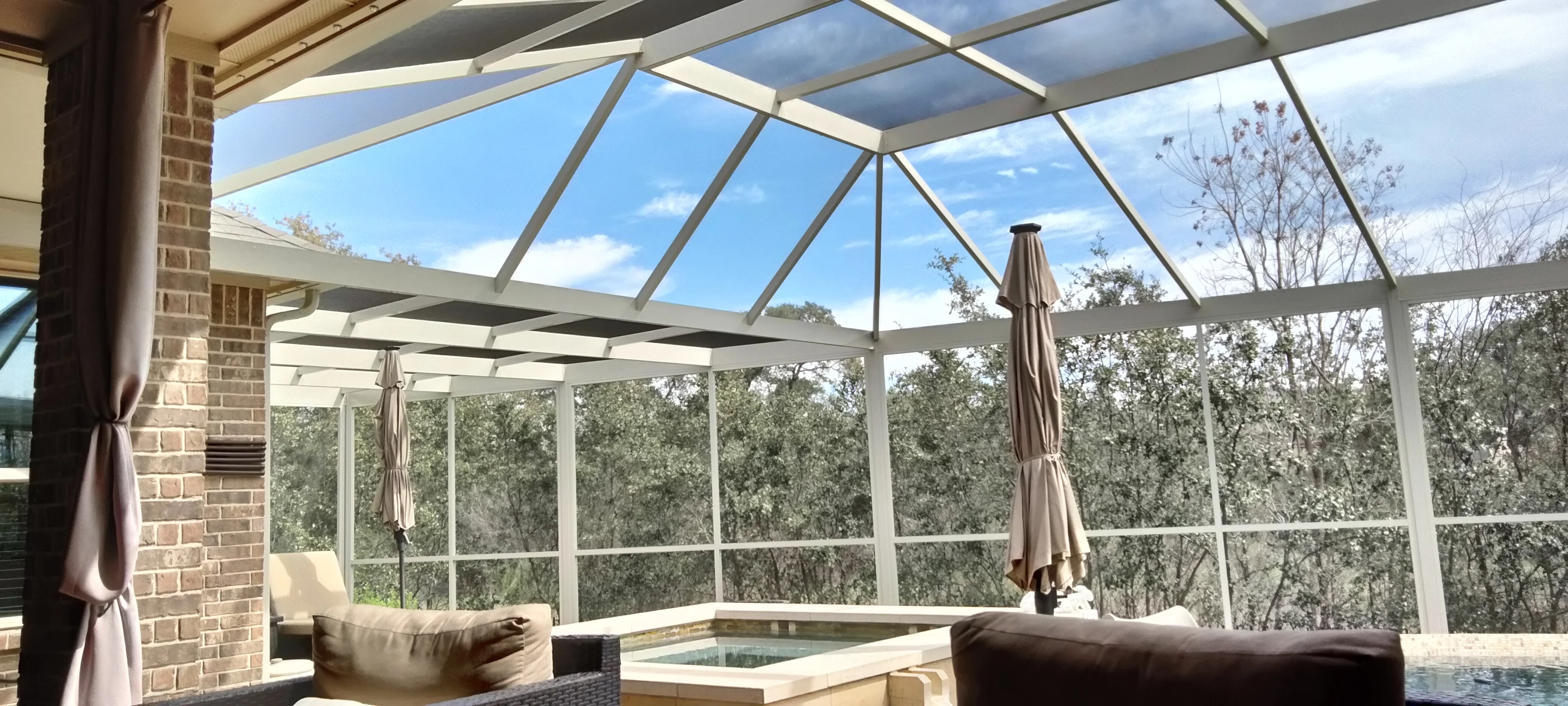 Glass patio enclosure with aluminum frame, gabled roof, and full-view glass panels overlooking trees