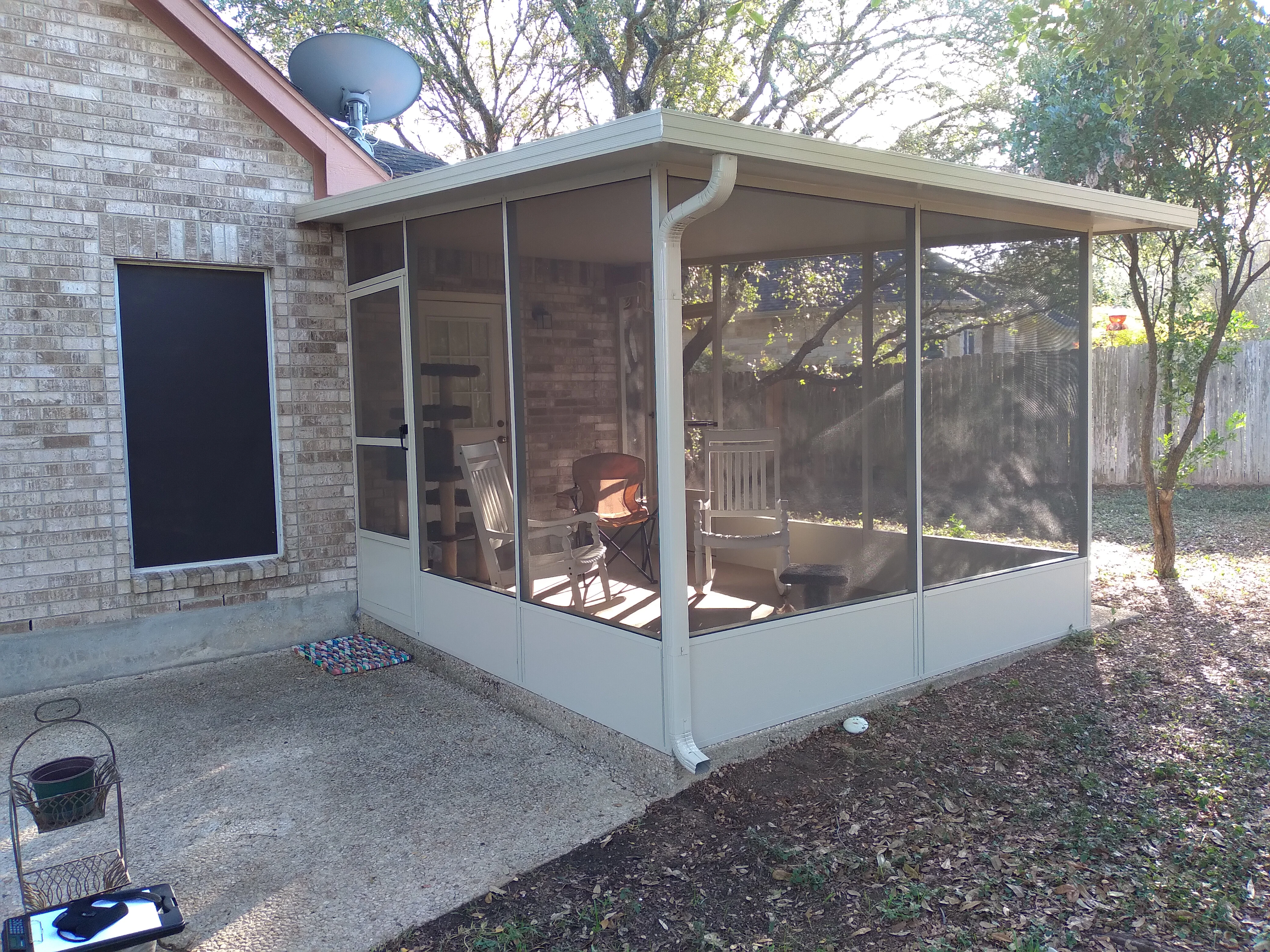 Aluminum-framed screened patio enclosure with gray knee wall and roof attached to brick house