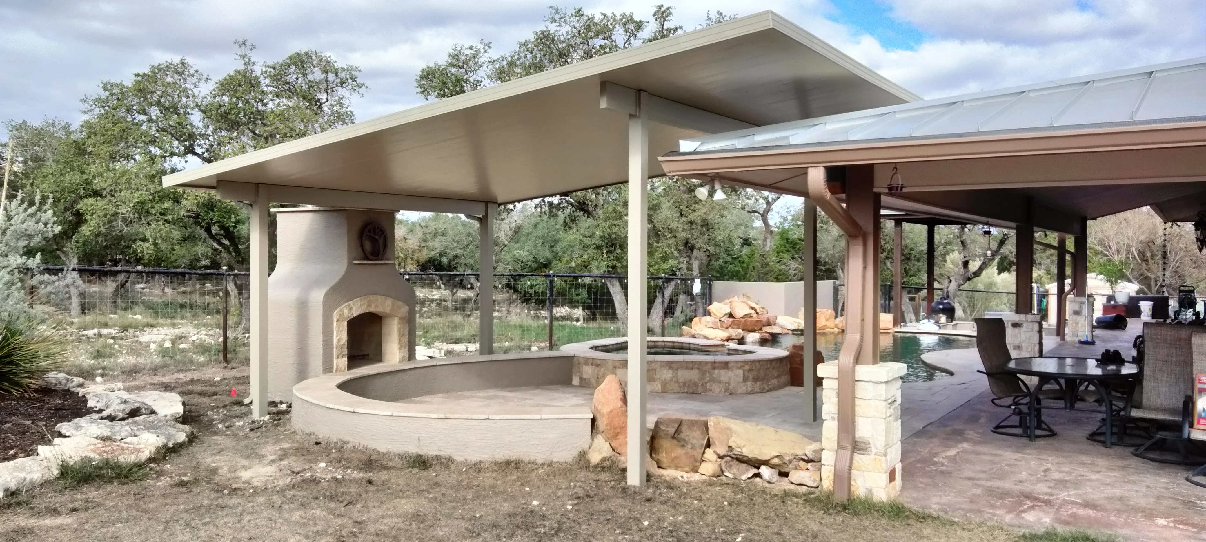 Freestanding patio cover with concrete roof, white columns, and circular fire pit surrounded by stone pillars