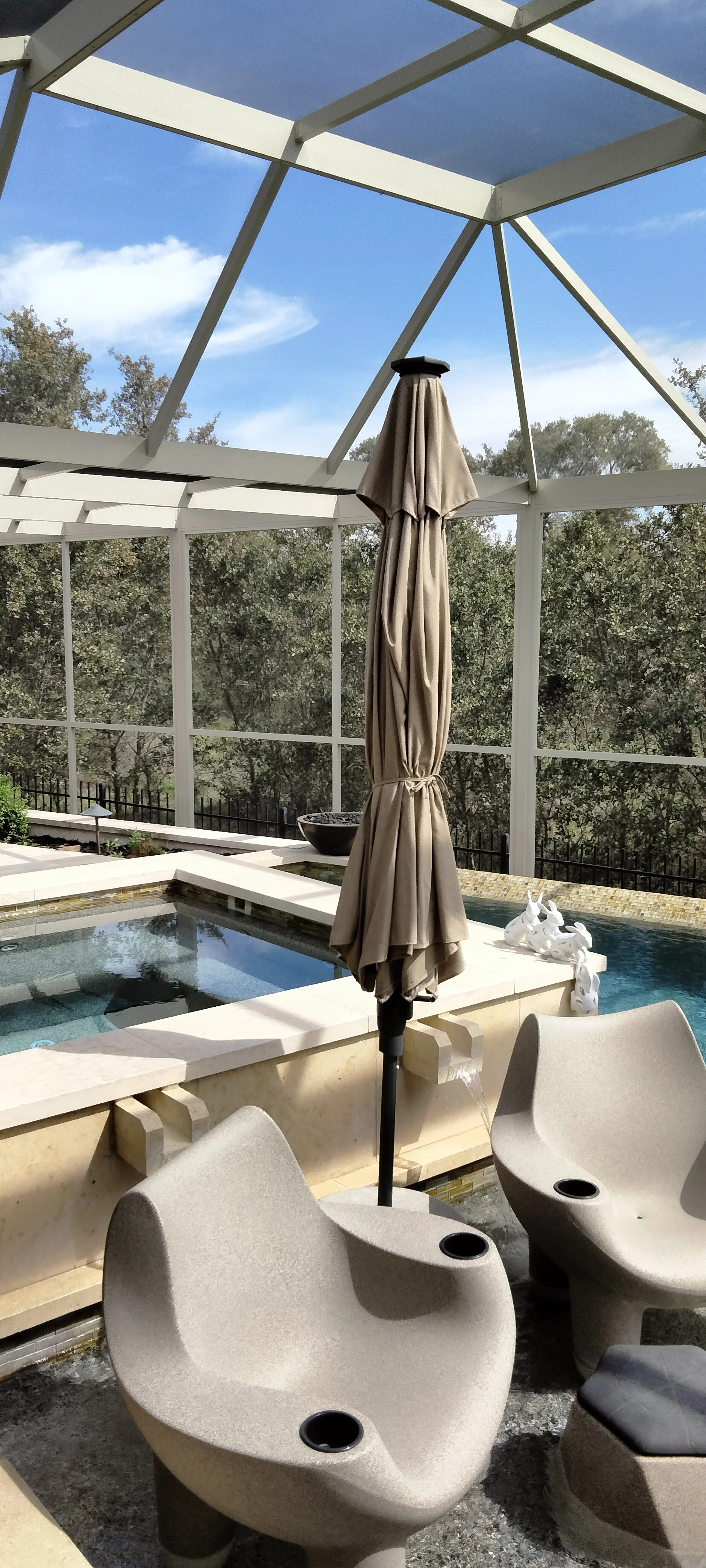 Aluminum patio enclosure with glass panels, concrete seating pods, and pool deck