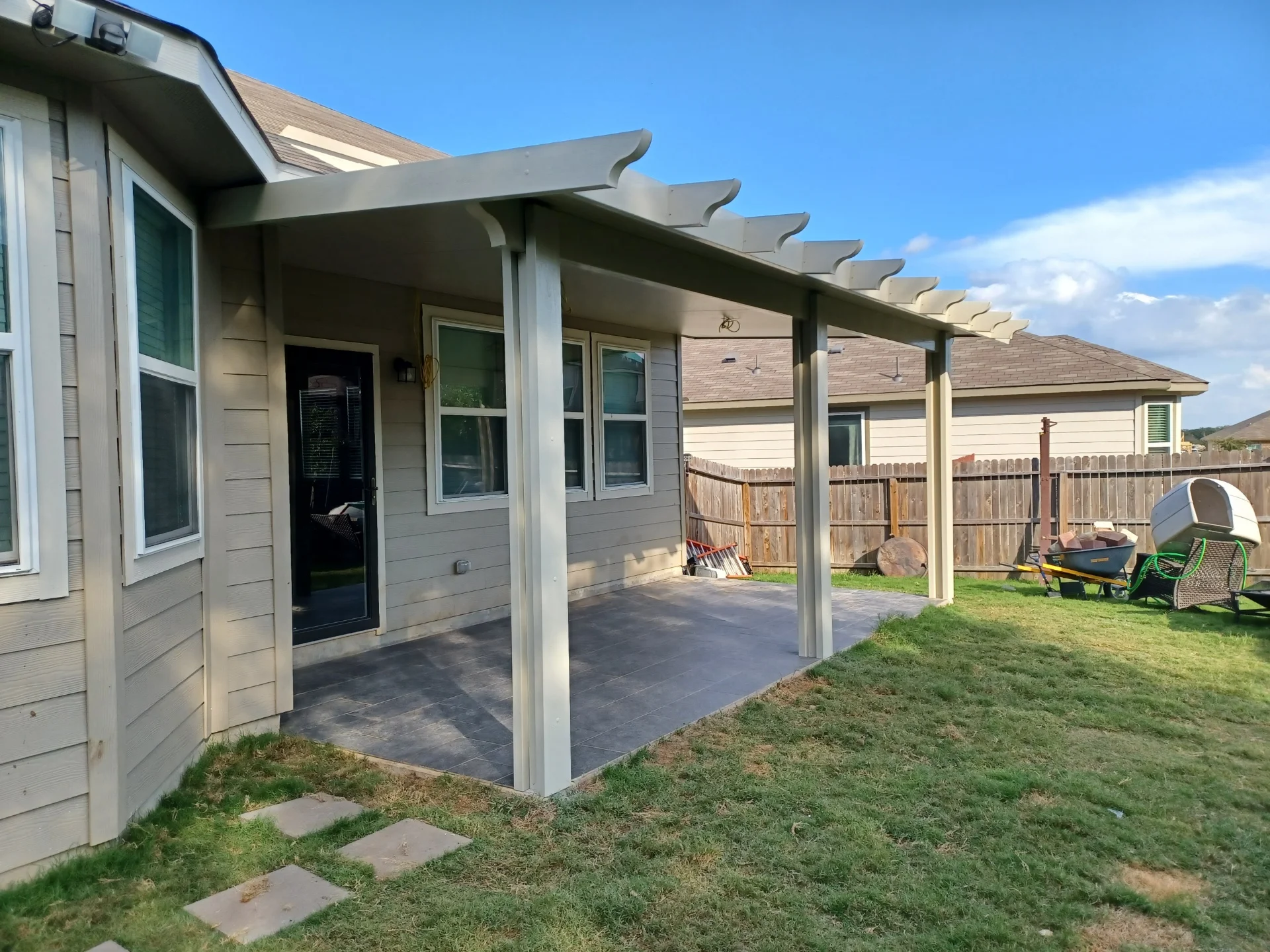 White aluminum patio cover with angled louvers over stamped concrete pad attached to house