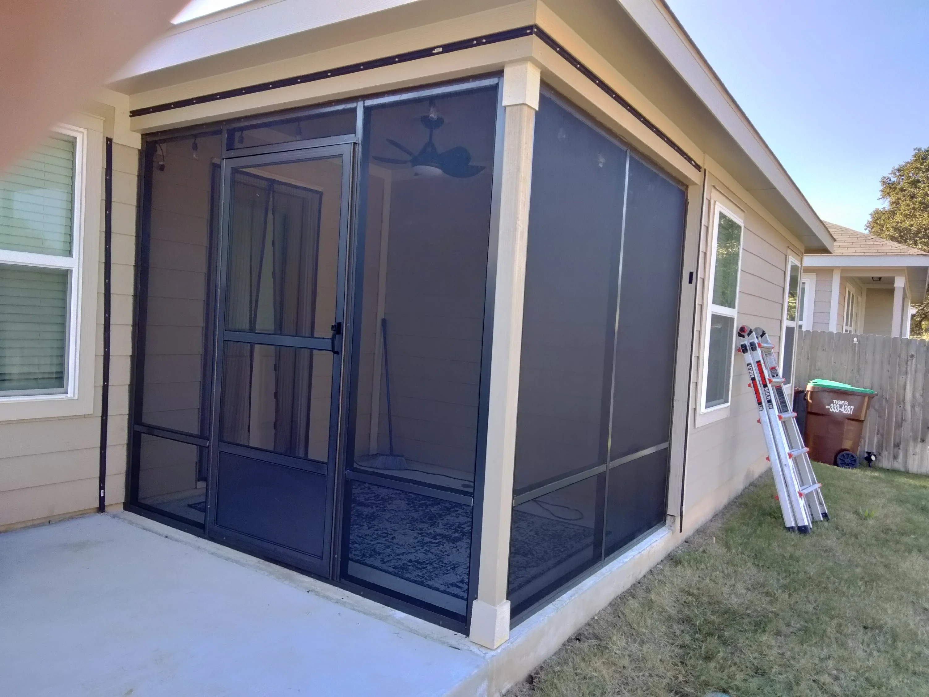 Black aluminum patio enclosure with sliding glass panels and entry door on concrete pad