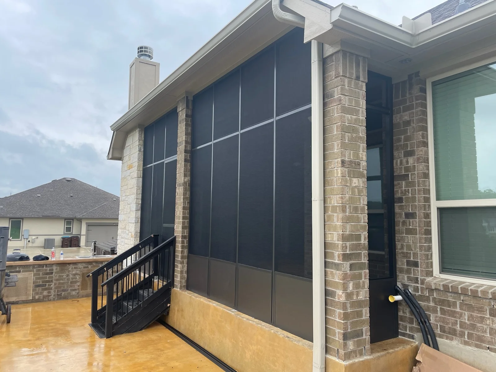 Brick patio enclosure with motorized mesh screens and aluminum frame on stamped concrete deck