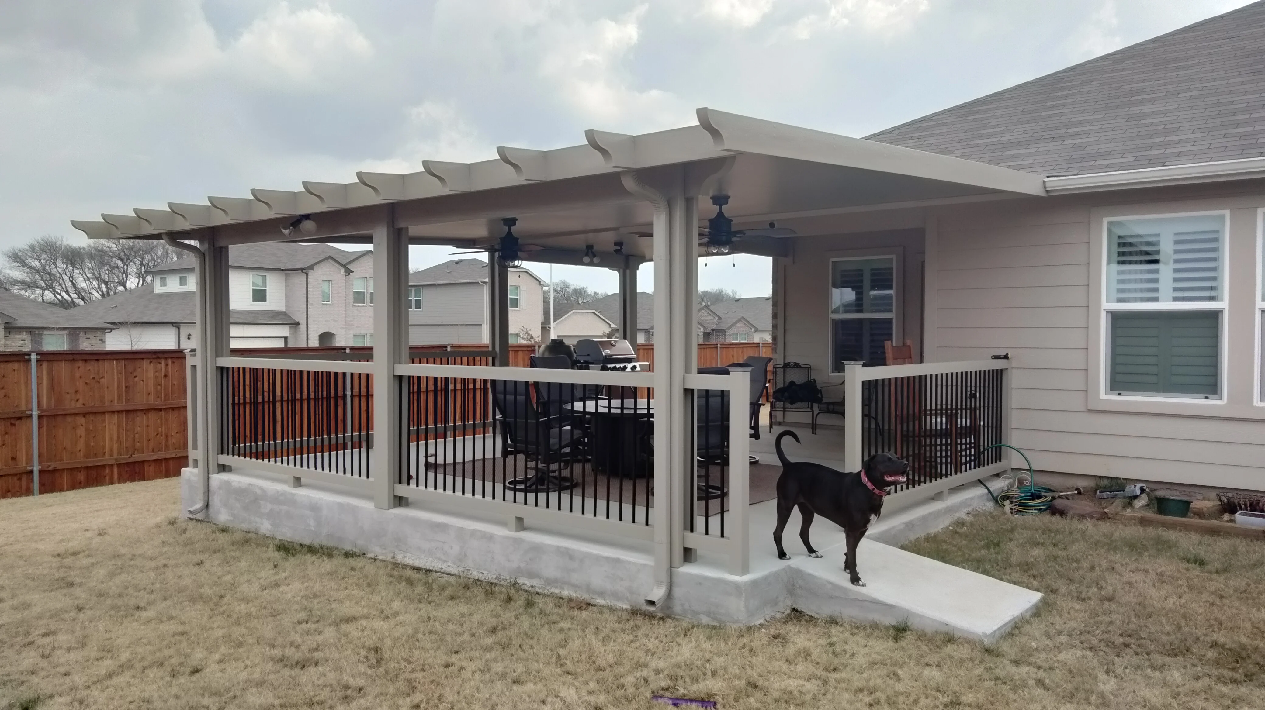 White aluminum patio enclosure with louvered roof, black metal railings, and concrete foundation