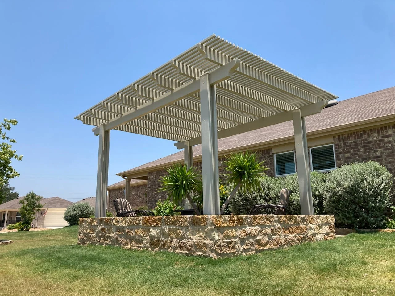 Steel pergola with horizontal slats over stone planter and patio seating area