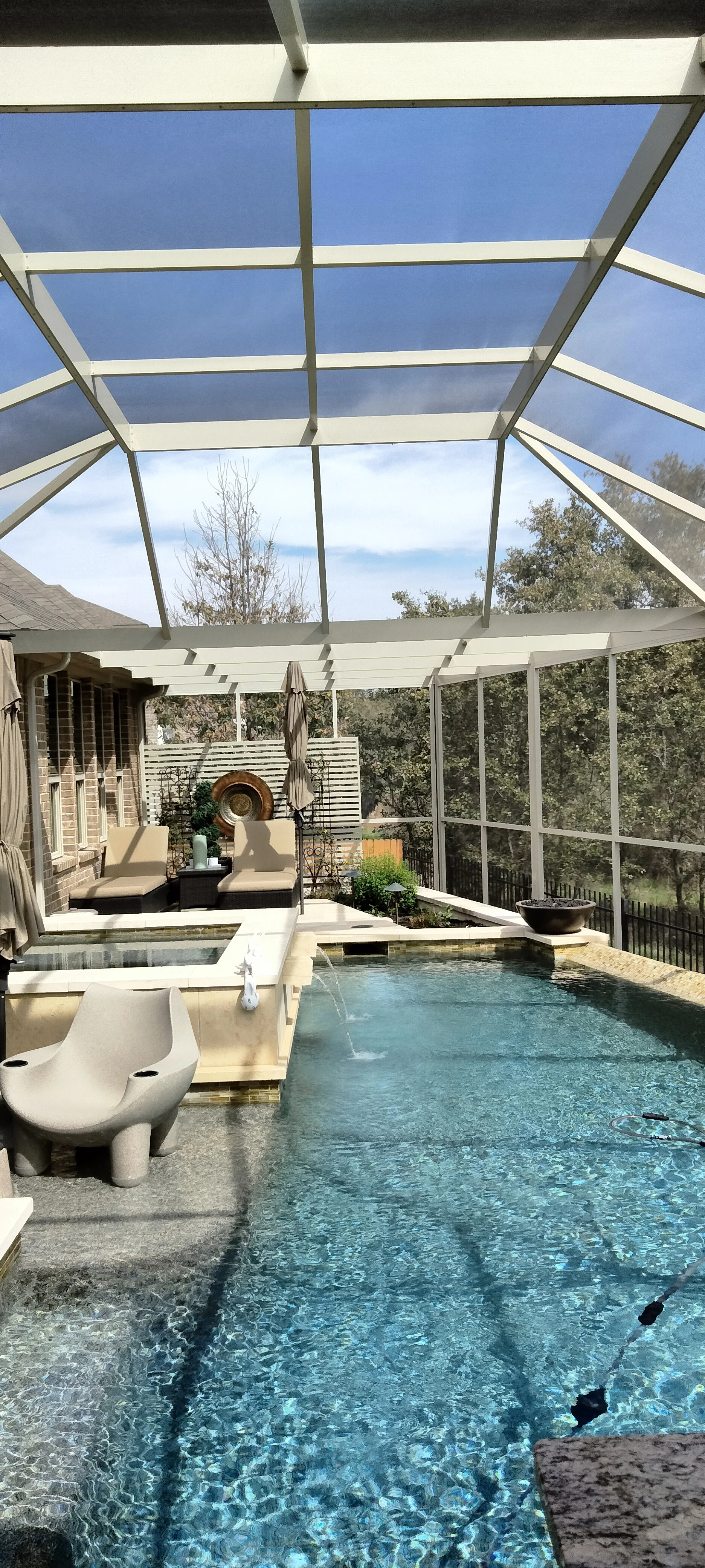 White aluminum glass patio enclosure with pool, lounge chairs, and stone decking