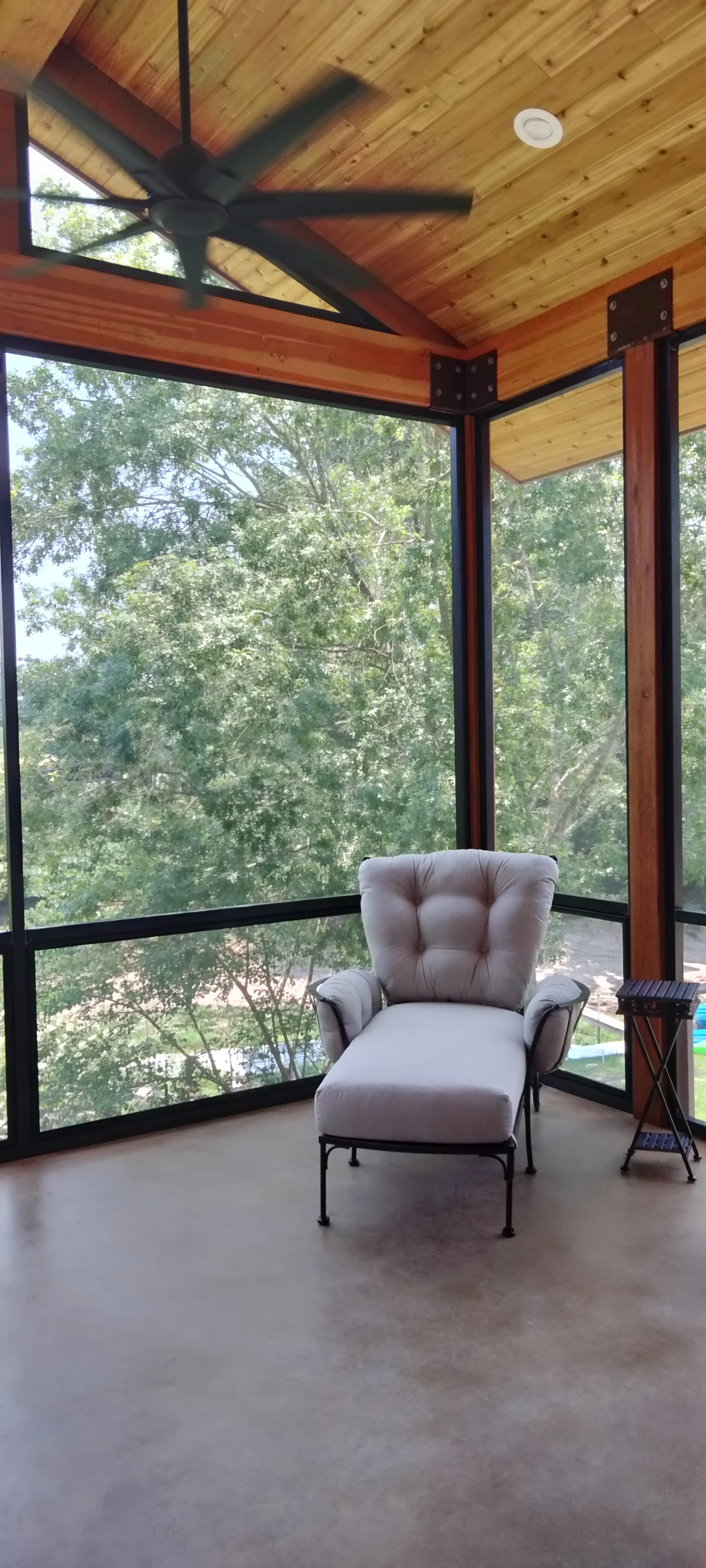 Sunroom interior with wood ceiling, black steel frame windows, and ceiling fan