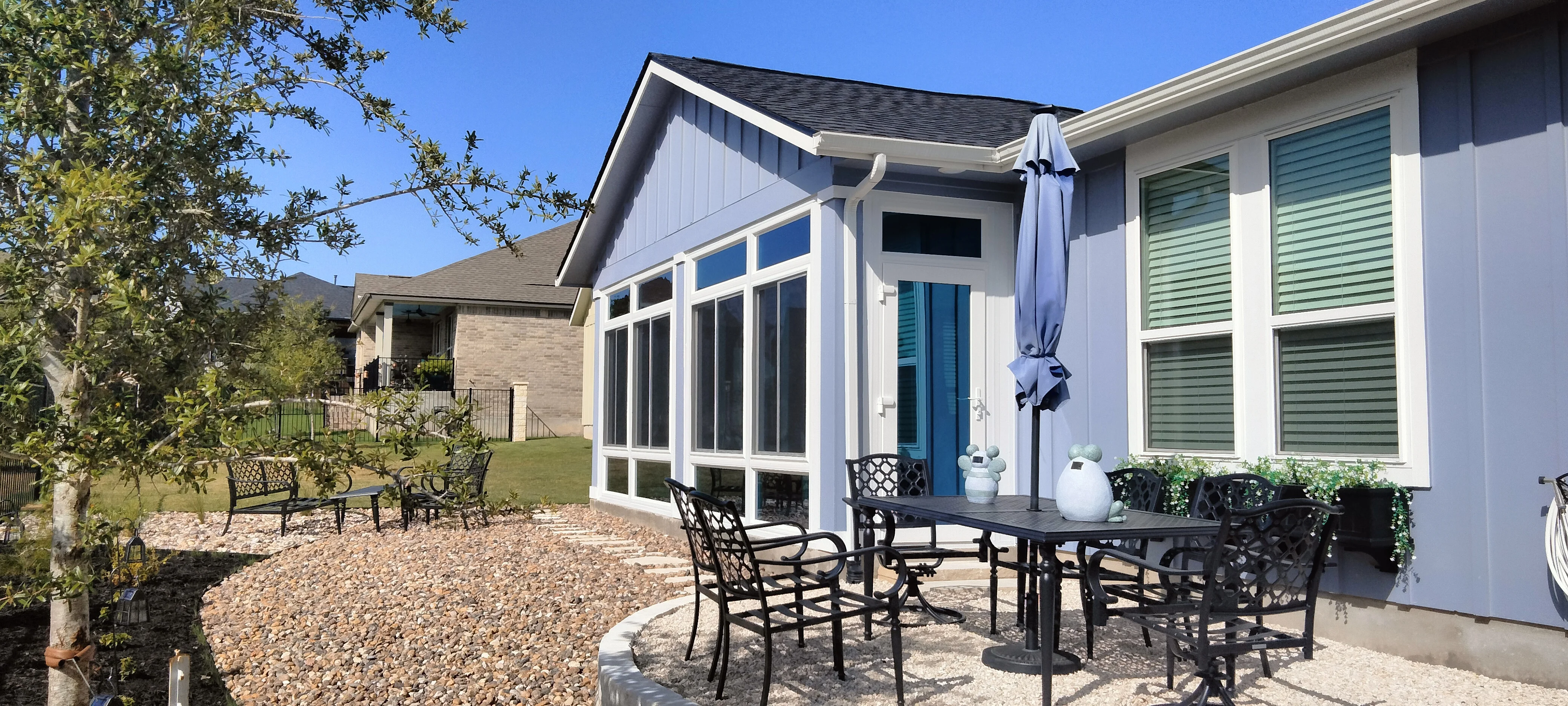 White sunroom with multi-pane windows and glass doors, adjacent patio with gravel and metal furniture