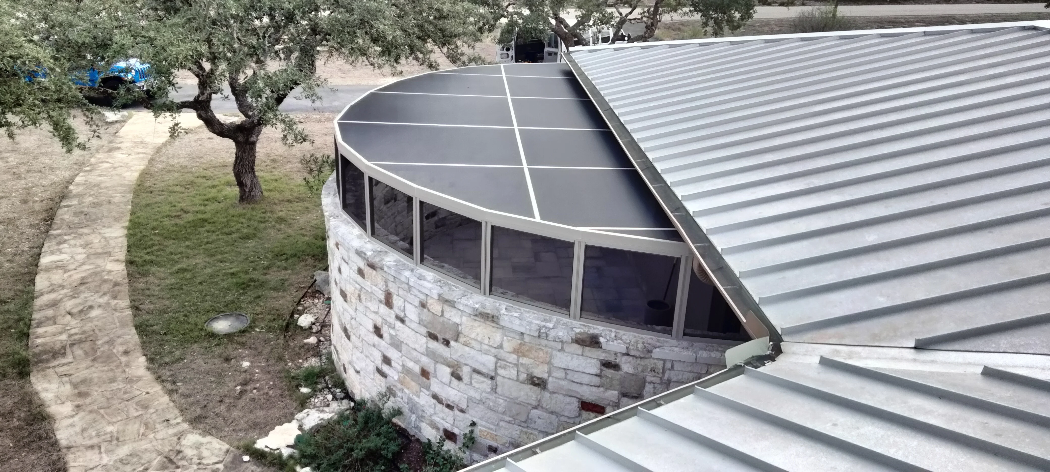 Curved sunroom with stone veneer walls, metal roof panels, and aluminum-framed windows