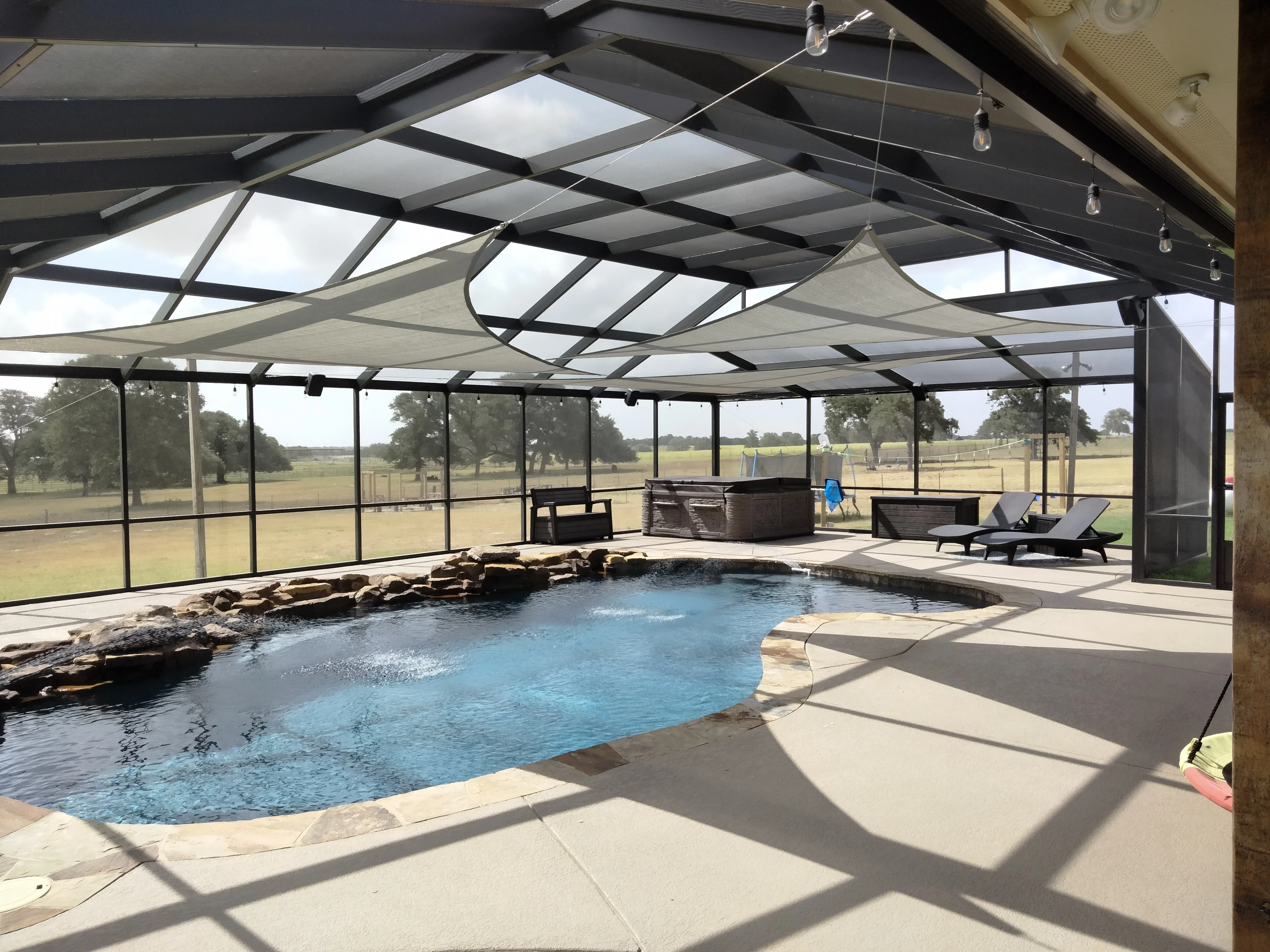 Screened pool enclosure with retractable shade, aluminum frame, concrete deck, and integrated fire pit seating area