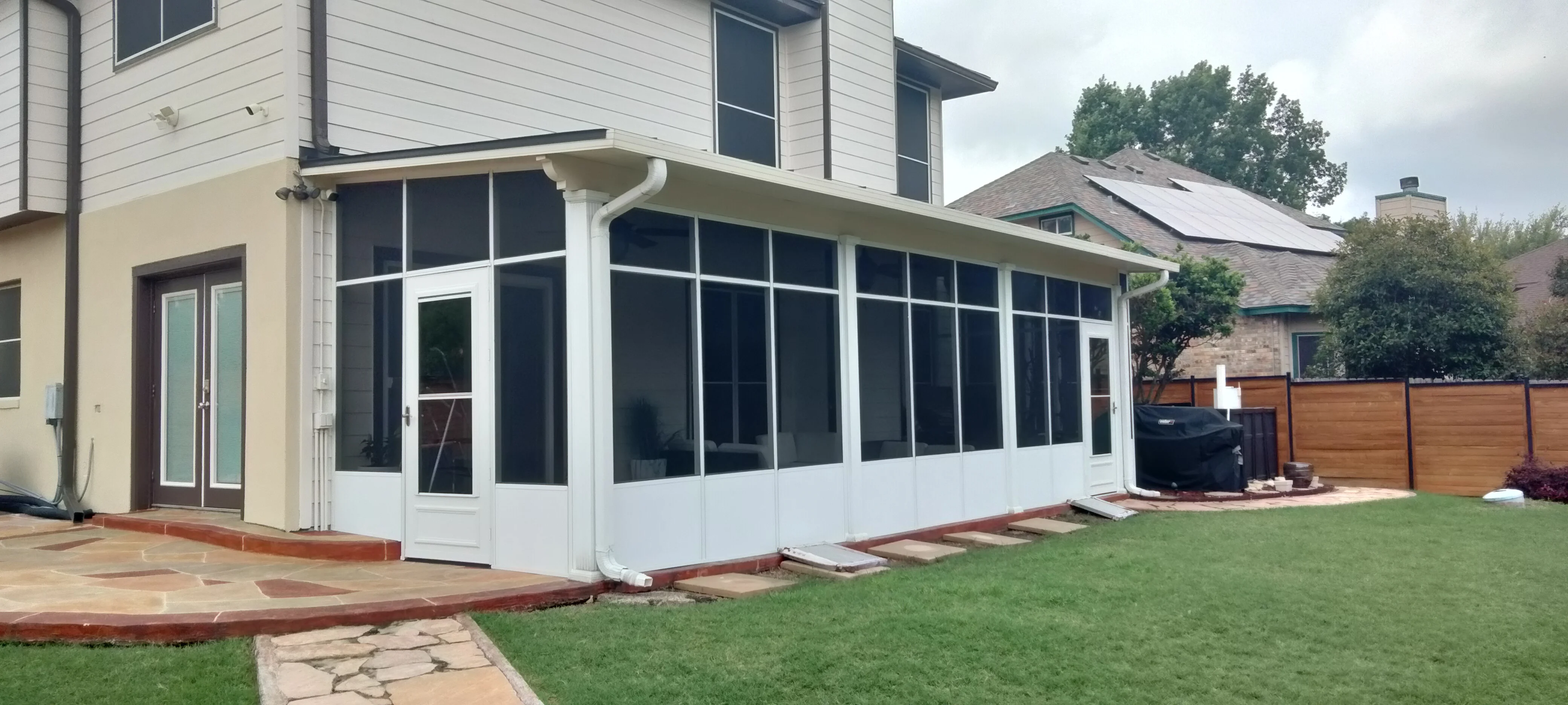 White aluminum patio enclosure with dark tinted glass panels and roof overhang