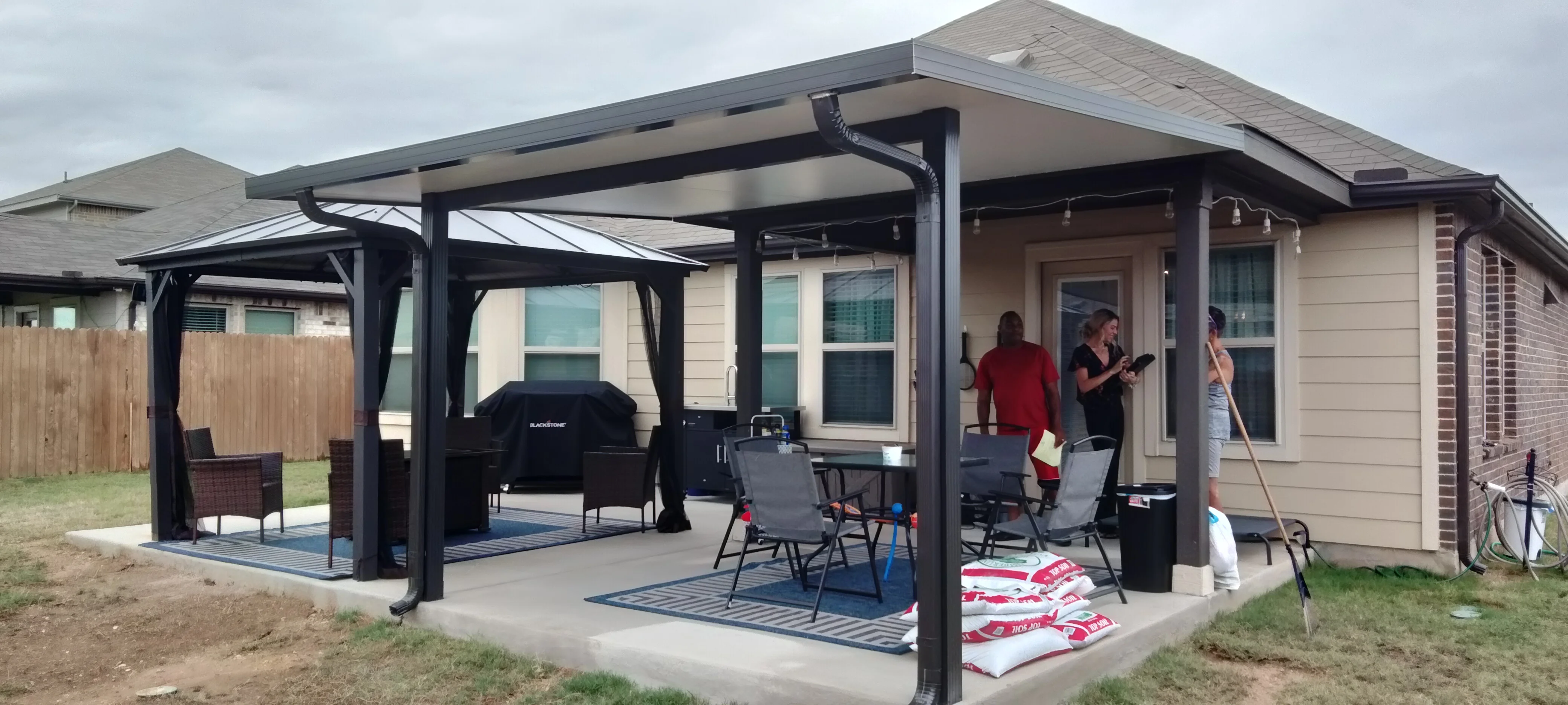 Black aluminum pergola with shade panels over concrete patio and seating area