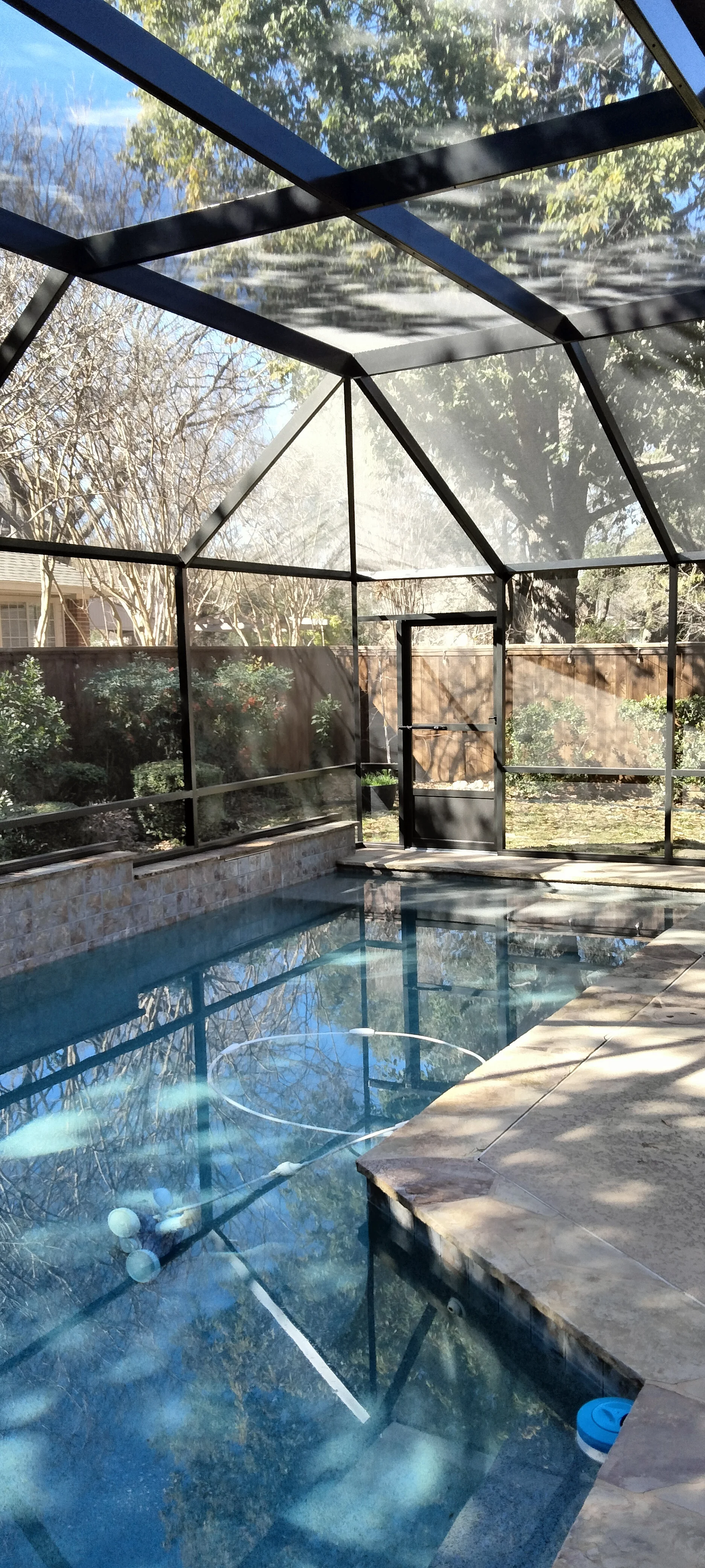 Aluminum pool enclosure with clear panels, peaked roof, and concrete deck surrounding in-ground pool