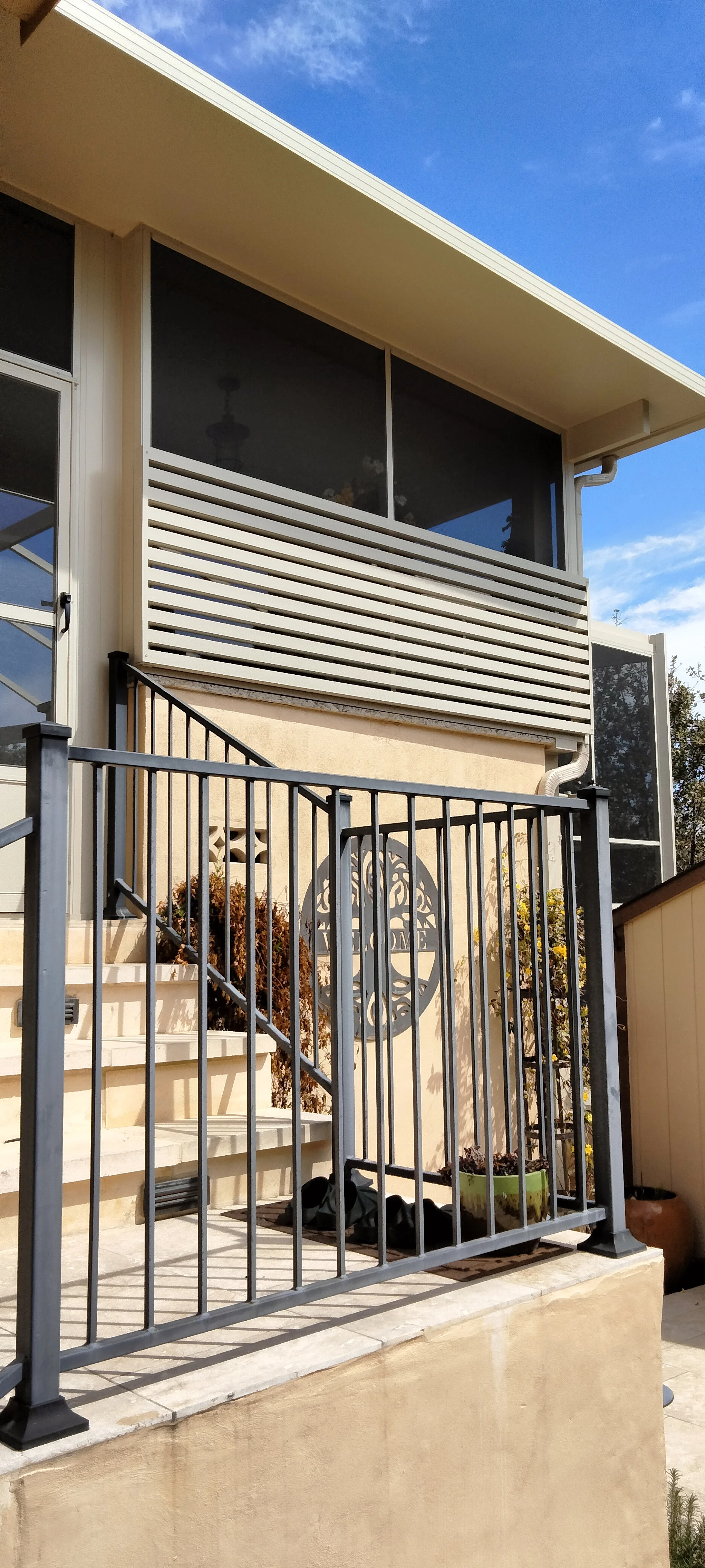 Patio enclosure with horizontal louvered aluminum screens, black metal railing, and fixed windows