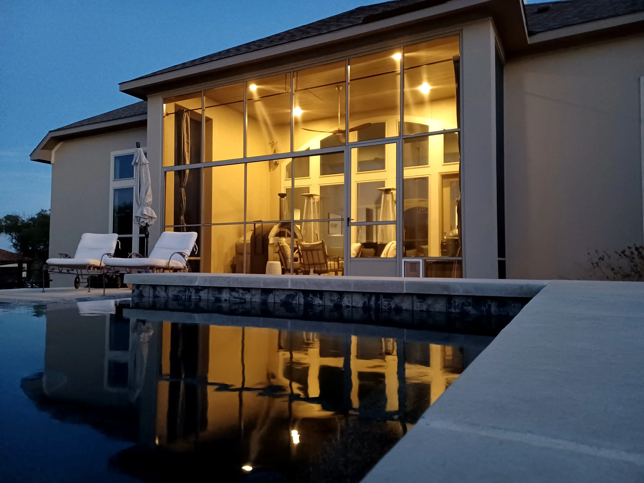 Glass patio enclosure with aluminum framing, polished concrete deck, and integrated lighting at dusk