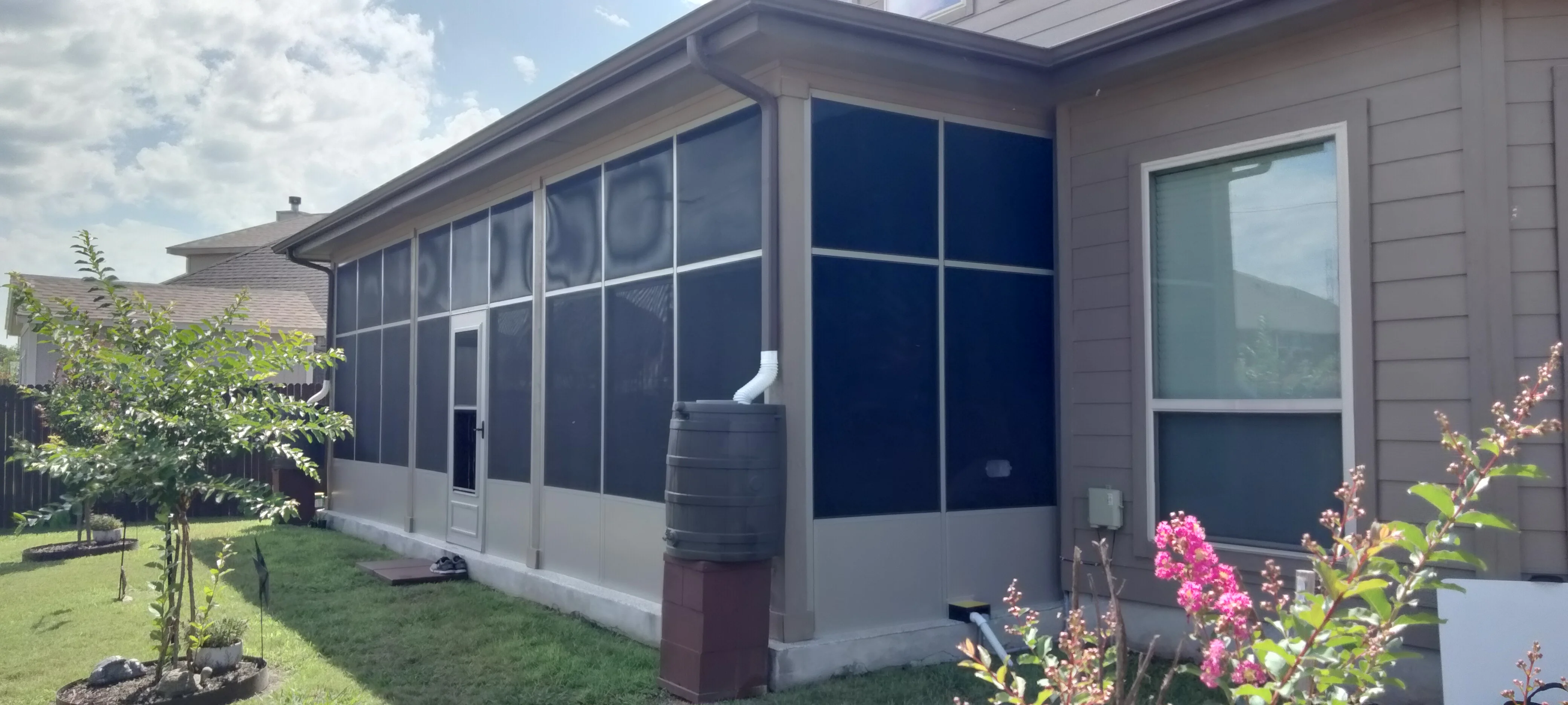 Aluminum-framed screened patio with dark mesh panels, white base, and gable roof attached to residential home