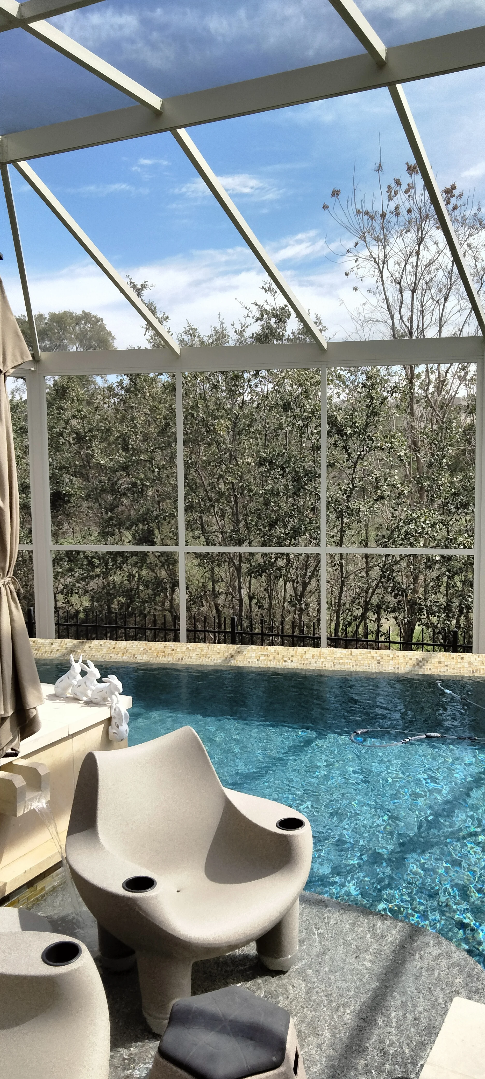 Glass sunroom with angled panels, white aluminum frame, and pool enclosure with brick decking