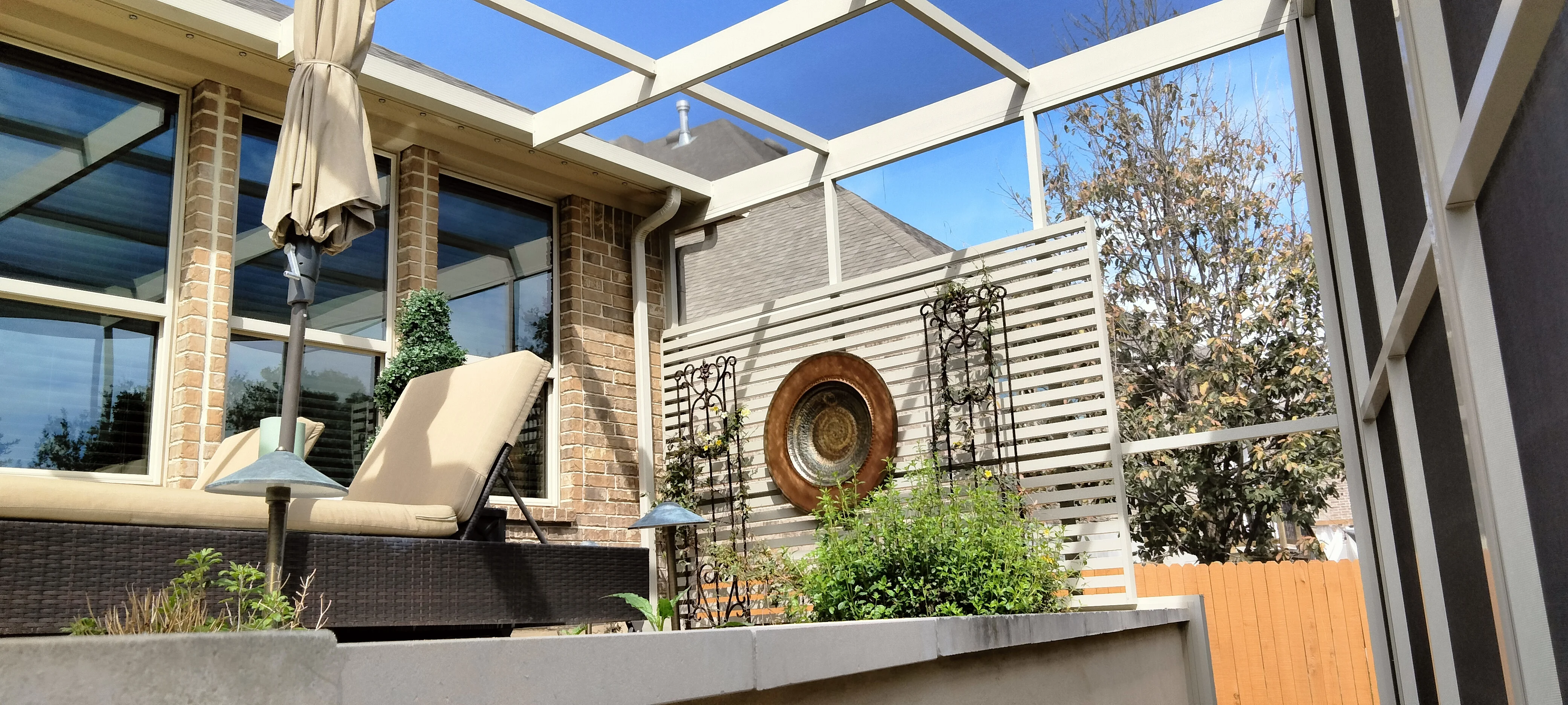 White pergola patio with horizontal slat screening, skylight panels, and concrete planters