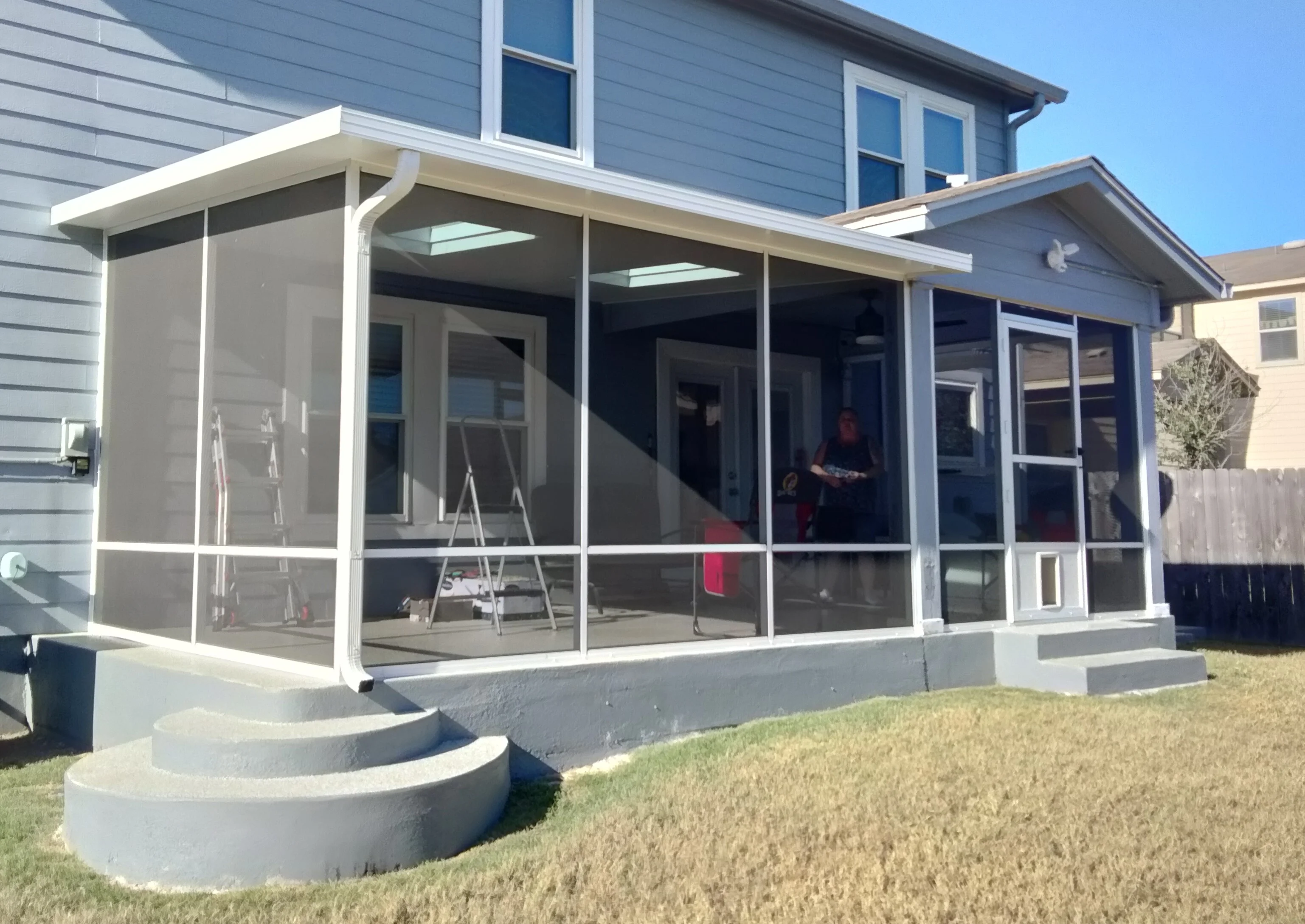 White aluminum patio enclosure with glass panels, skylights, and curved concrete steps