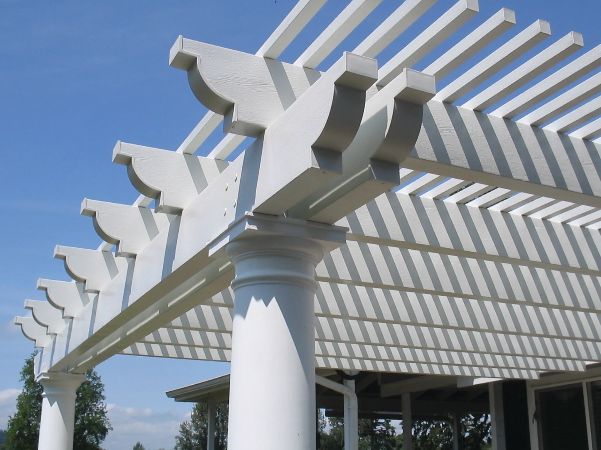 White Alumawood pergola with lattice beams and curved decorative brackets on cylindrical post