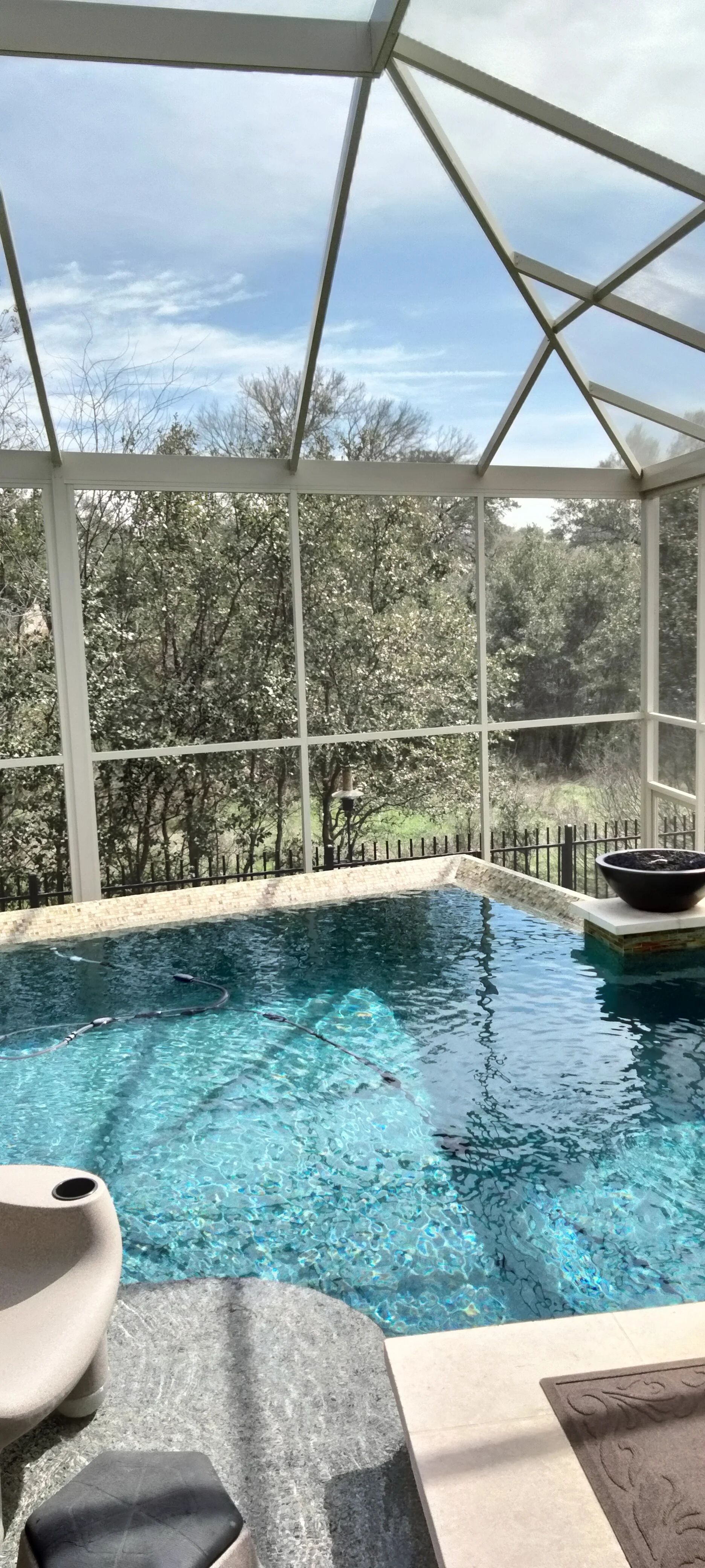 Aluminum screened pool enclosure with gable roof, turquoise tile pool, concrete deck, and metal fencing