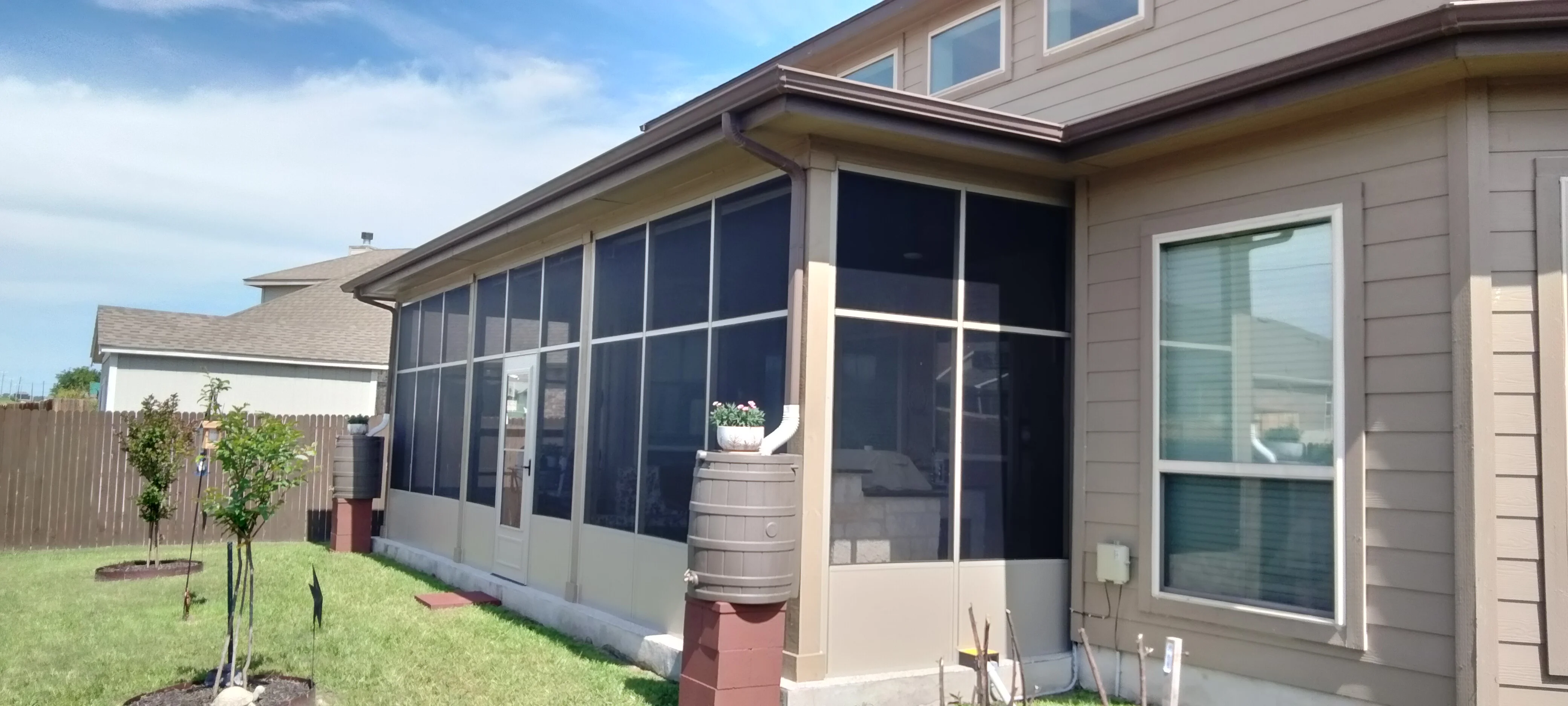 Aluminum-framed screened patio with dark mesh panels and white base trim attached to home
