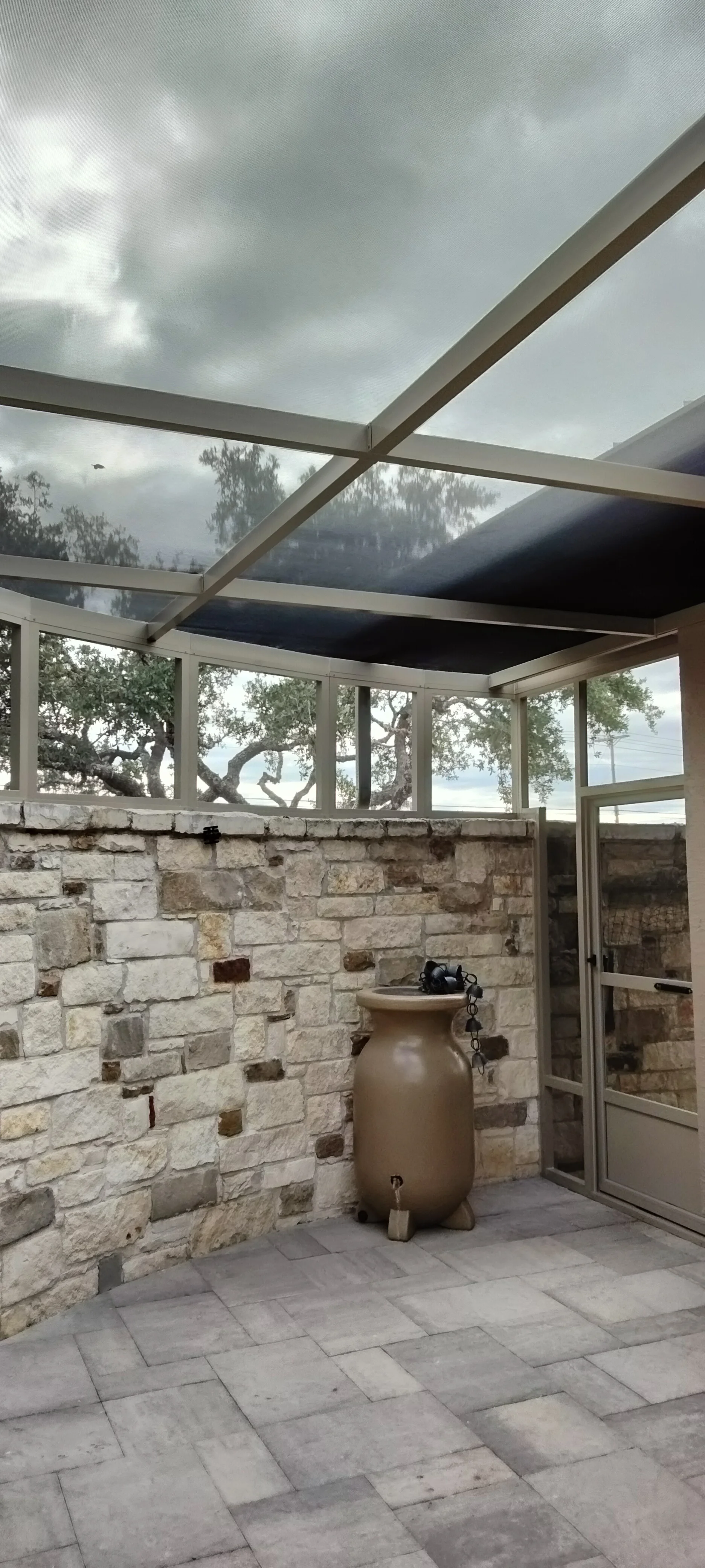 Aluminum patio enclosure with glass panels, stone veneer walls, and retractable shade