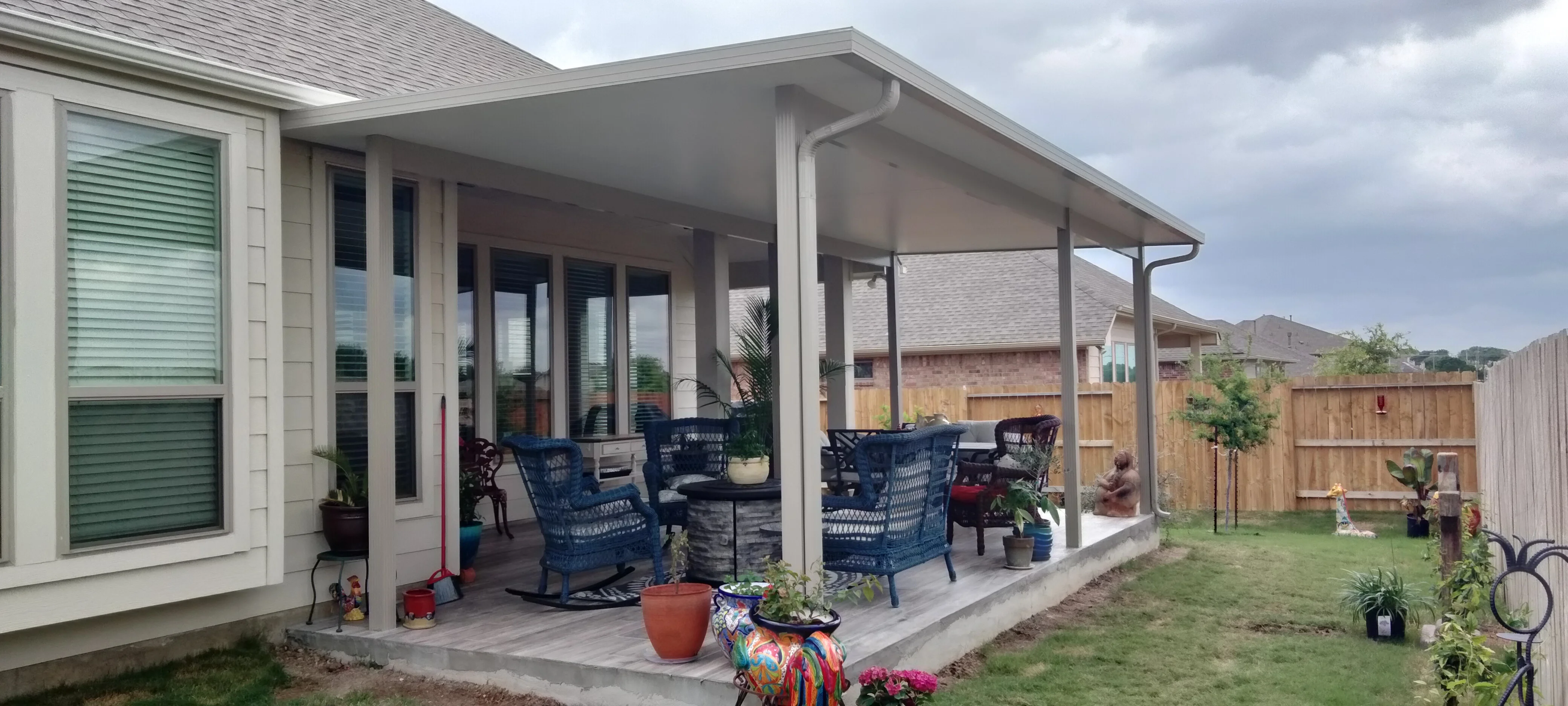 White gable roof patio with concrete pad, columns, and blue seating furniture